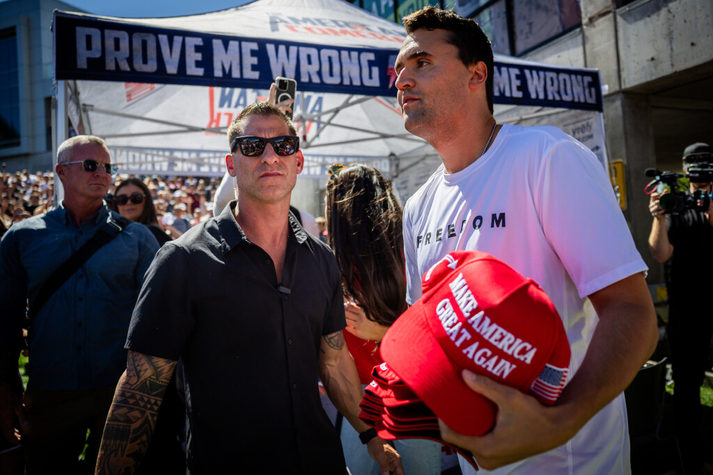 Charlie Kirk’s, the CEO and co-founder of the conservative youth organization Turning Point USA, security guard, left, stands by as Kirk hands out hats before Kirk is fatally shot during Turning Point USA’s visit to Utah Valley University in Orem on Wednesday, Sept. 10, 2025.