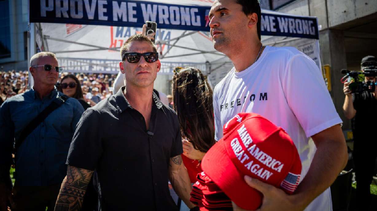 Charlie Kirk’s, the CEO and co-founder of the conservative youth organization Turning Point USA, security guard, left, stands by as Kirk hands out hats before Kirk is fatally shot during Turning Point USA’s visit to Utah Valley University in Orem on Wednesday, Sept. 10, 2025.