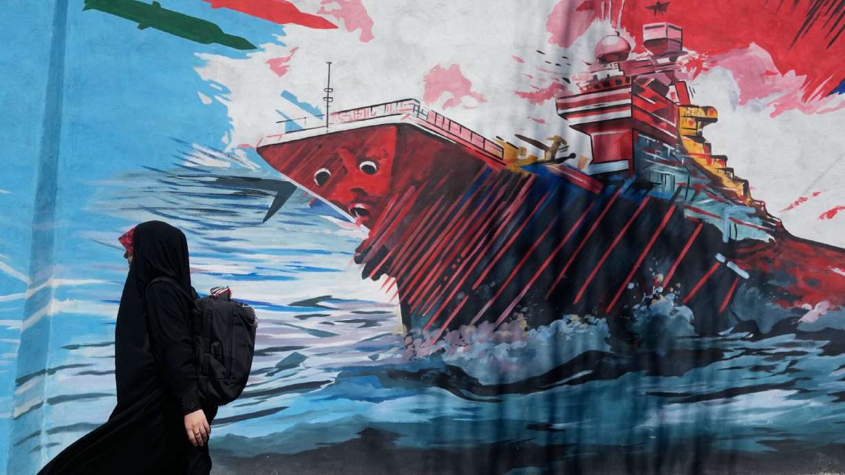 A woman walks past a mural depicting a U.S. aircraft carrier under missile attack in downtown Tehran, Iran, Monday, June 8, 2026.