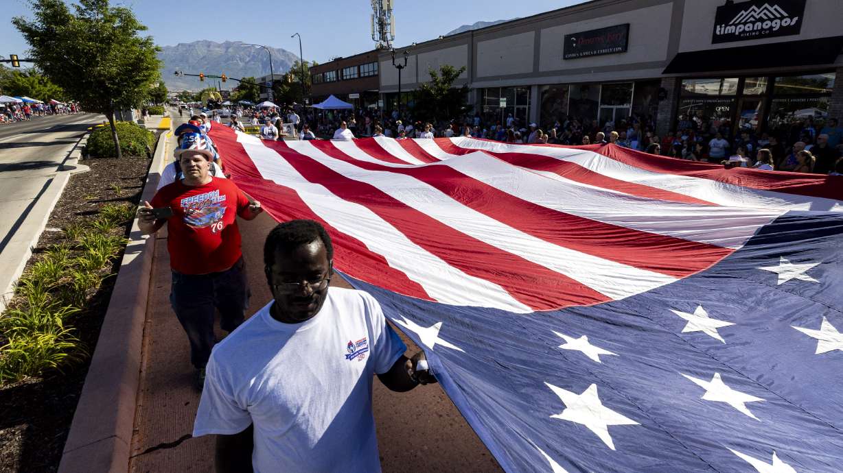 People hold open an American flag as they walk during the Freedom Festival Grand Parade held along University Avenue in Provo on Saturday. Hundreds of thousands gathered for the parade, one of the largest 4th of July parades in the western U.S.