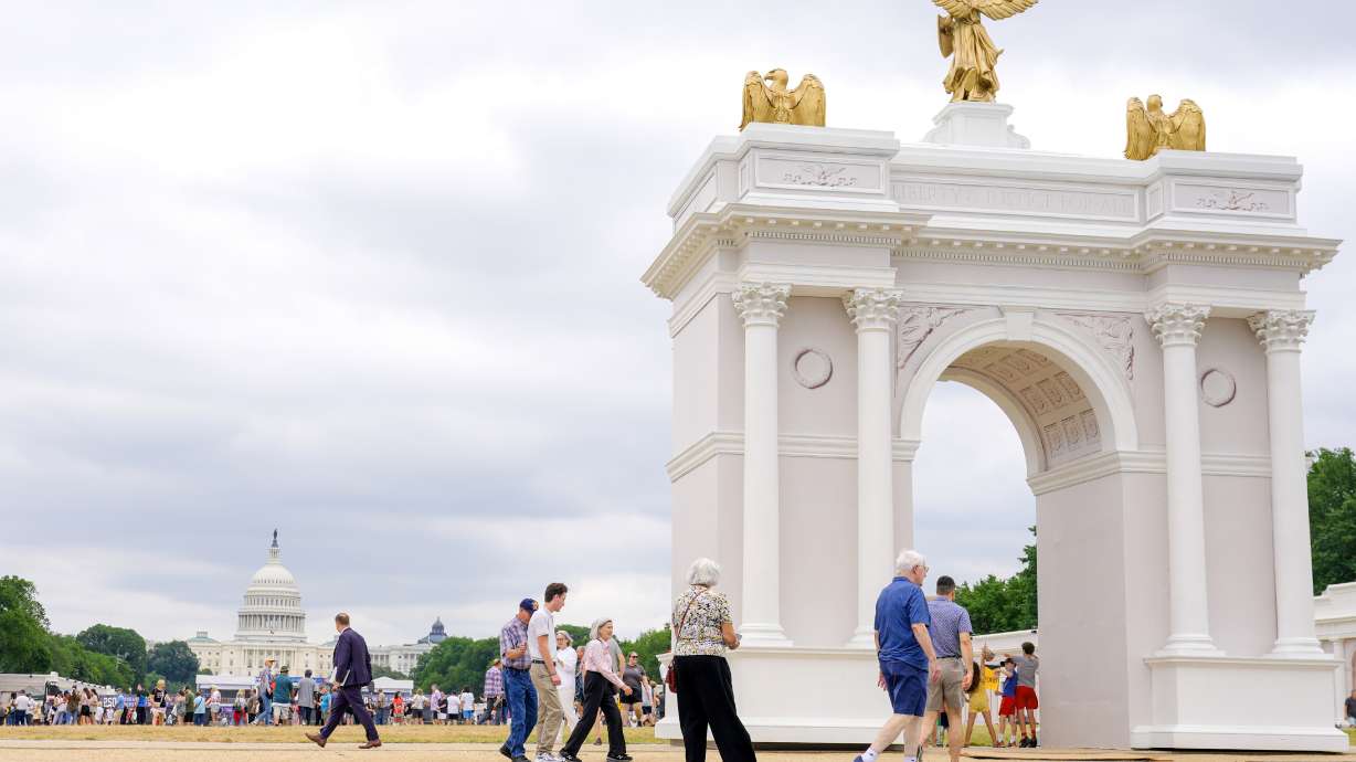 Visitors walk at the Great American State Fair with the triumphal arch model and the U.S. Capitol, in the background, Wednesday in Washington.