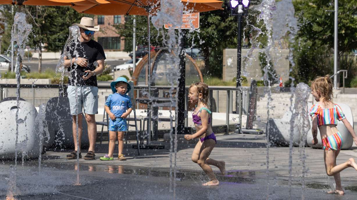 A boy patiently waits beside his father as he looks towards the other children playing at the Millcreek Commons splash pad in Millcreek on Sunday. Record-breaking heat impacted Utah this weekend, led by Salt Lake City's new all-time record of 109 degrees.