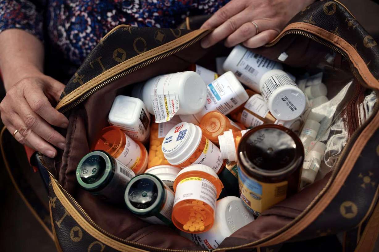 Sandy Lusty holds a bag of her medications and supplements in front of her home in Kaysville on July 1. Sandy has had to skip doses of prescription medication due to high costs. They each take more than a dozen prescription medications.