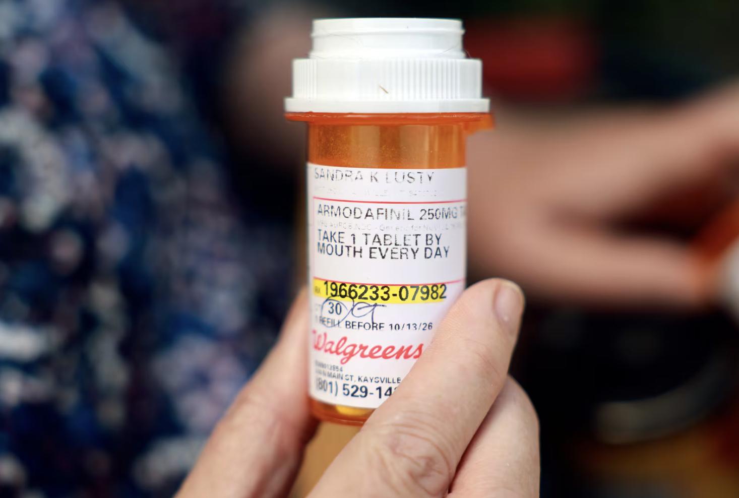Sandy Lusty holds a bottle of armodafinil in front of her home in Kaysville on July 1. Sandy has had to skip doses armodafinil due to high costs. She takes 17 prescription medications.