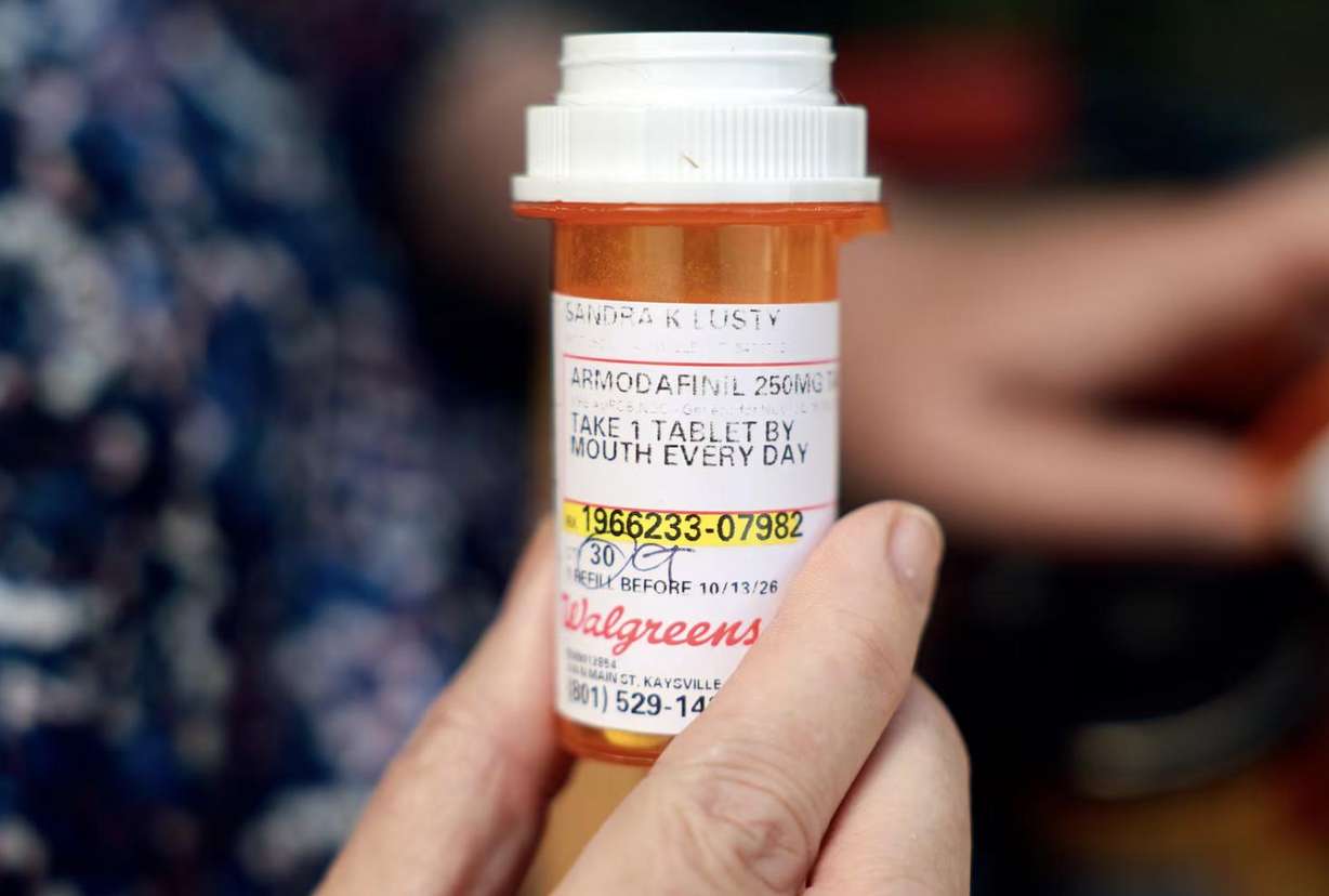 Sandy Lusty holds a bottle of armodafinil in front of her home in Kaysville on July 1. Sandy has had to skip doses armodafinil due to high costs. She takes 17 prescription medications.