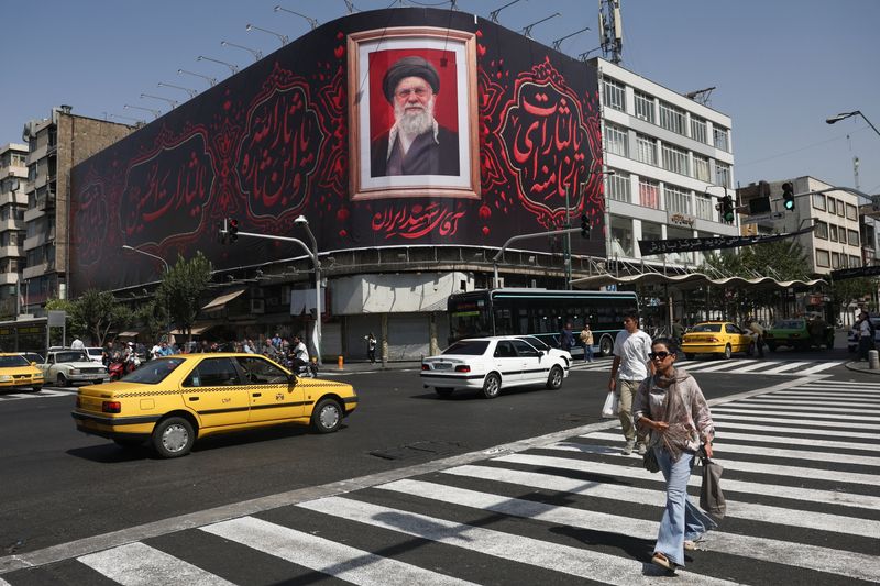 People walk past a billboard with an image of Iran's late Supreme Leader Ayatollah Ali Khamenei in Tehran, Iran, Monday. Iran launched more strikes on U.S. air bases in the Middle East on Tuesday.