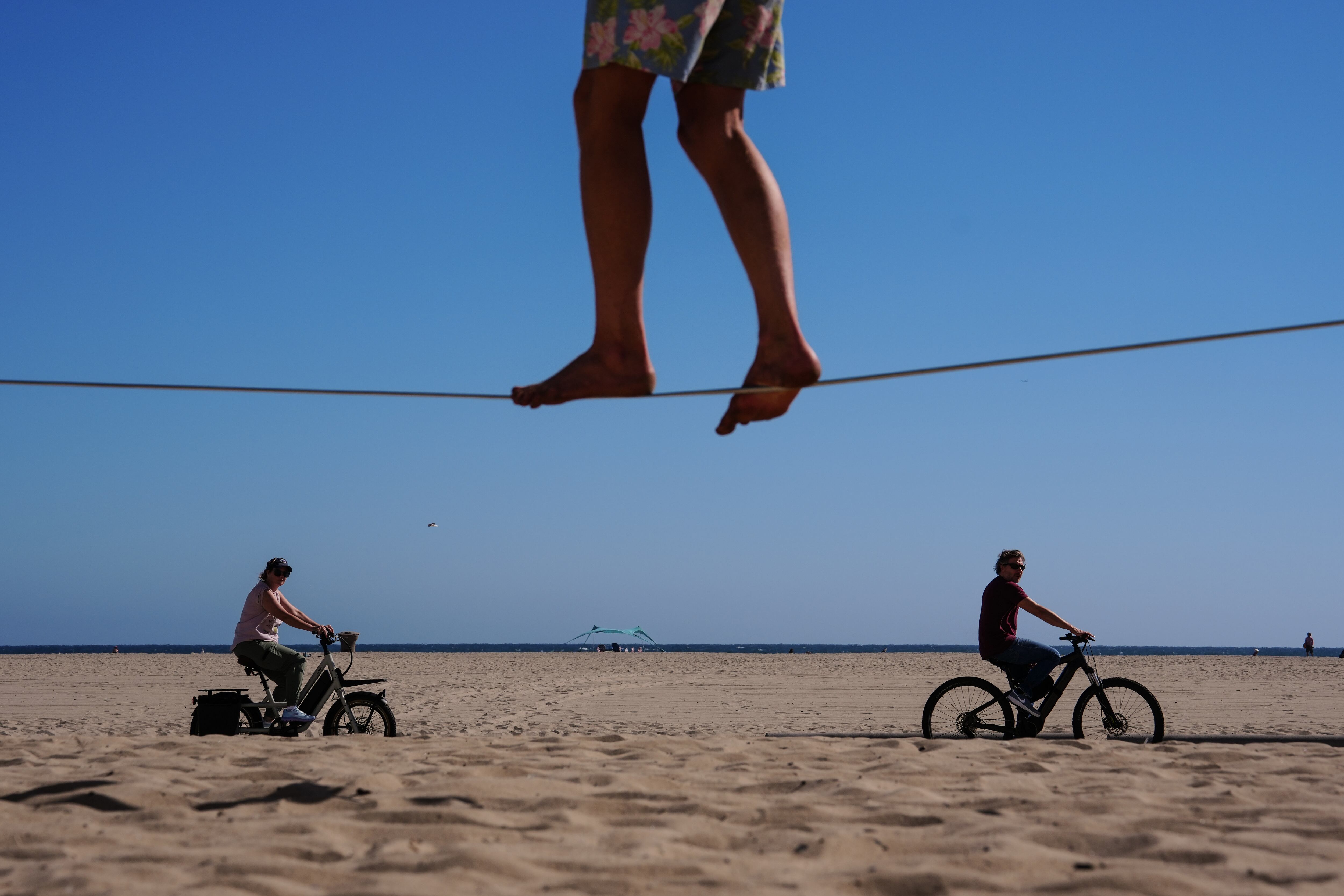 Two people ride bicycles along a beach path as a man balances on a slackline in Santa Monica, Calif., July 8.