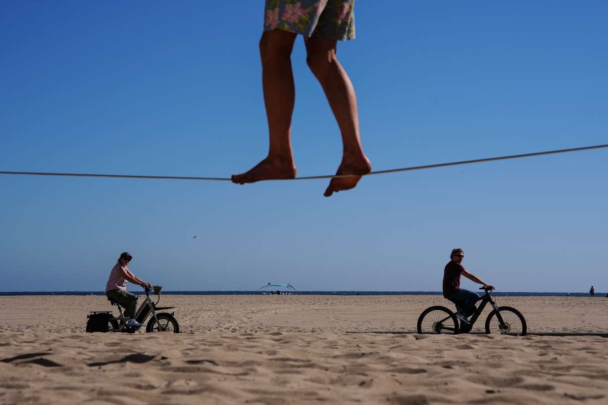 Two people ride bicycles along a beach path as a man balances on a slackline in Santa Monica, Calif., July 8.