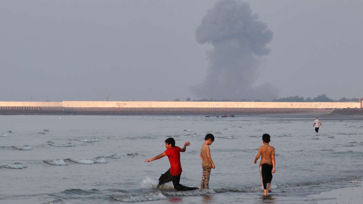 Three boys play in the shallow waters of the Strait of Hormuz, as a plume of smoke rises from an explosion in the background, off Bandar Abbas, Iran, Monday. The U.S. expanded its strikes on Iran on Thursday and disabled a ship trying to run its blockade.