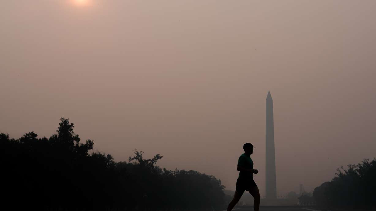 The sun is obscured by wildfire smoke as a person runs in front of the Washington Monument and Lincoln Memorial Reflecting Pool, Friday on the National Mall in Washington.
