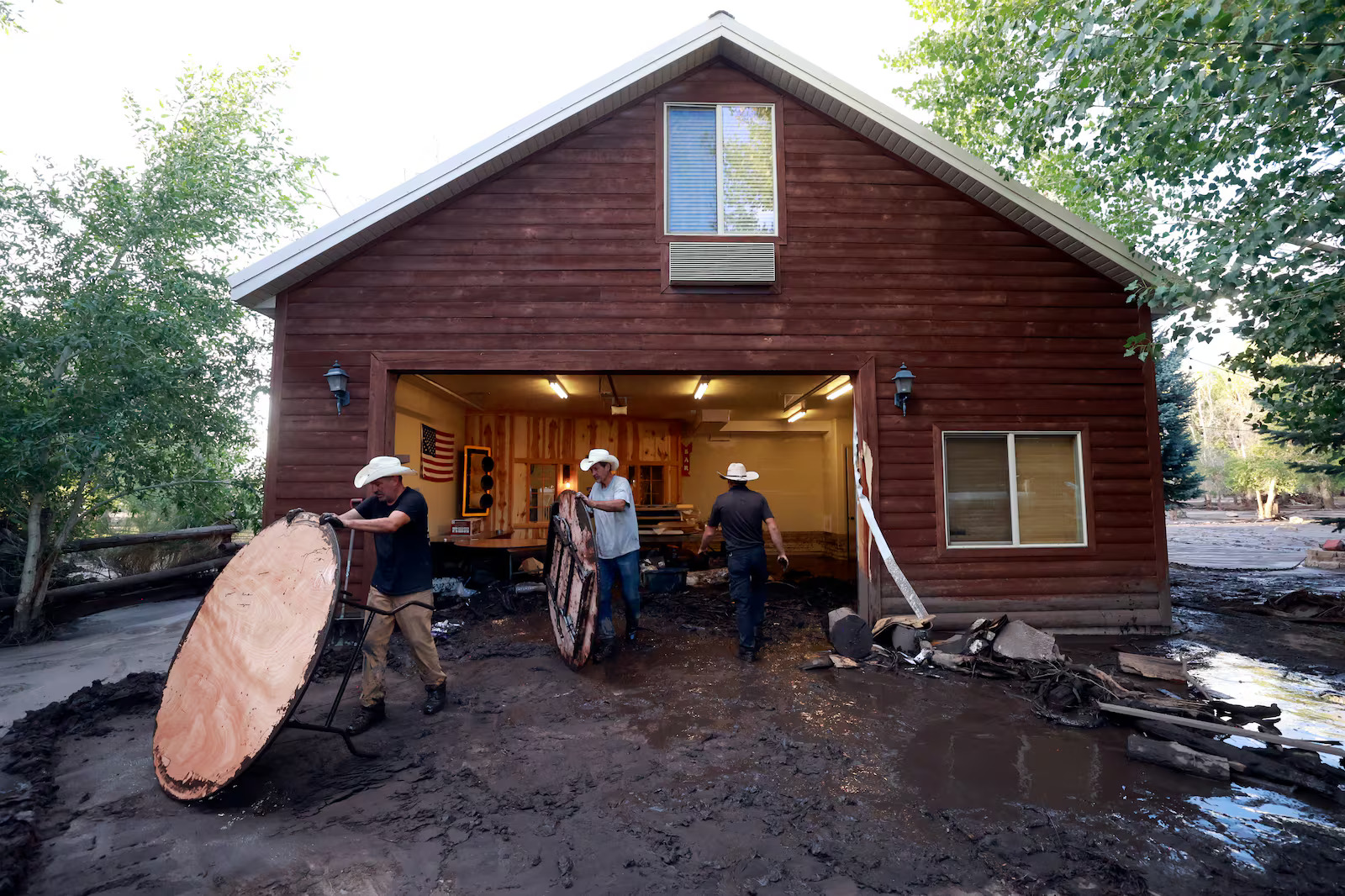Aaron Richardson, Curtis Street and Trendon Delray clean out Richardson’s flooded garage after flooding in Beaver on Monday. Richardson stored furniture for the Beaver River Ranch Wedding and Event Center in the garage, including the tables covered in mud. He still plans to host a wedding in early August.