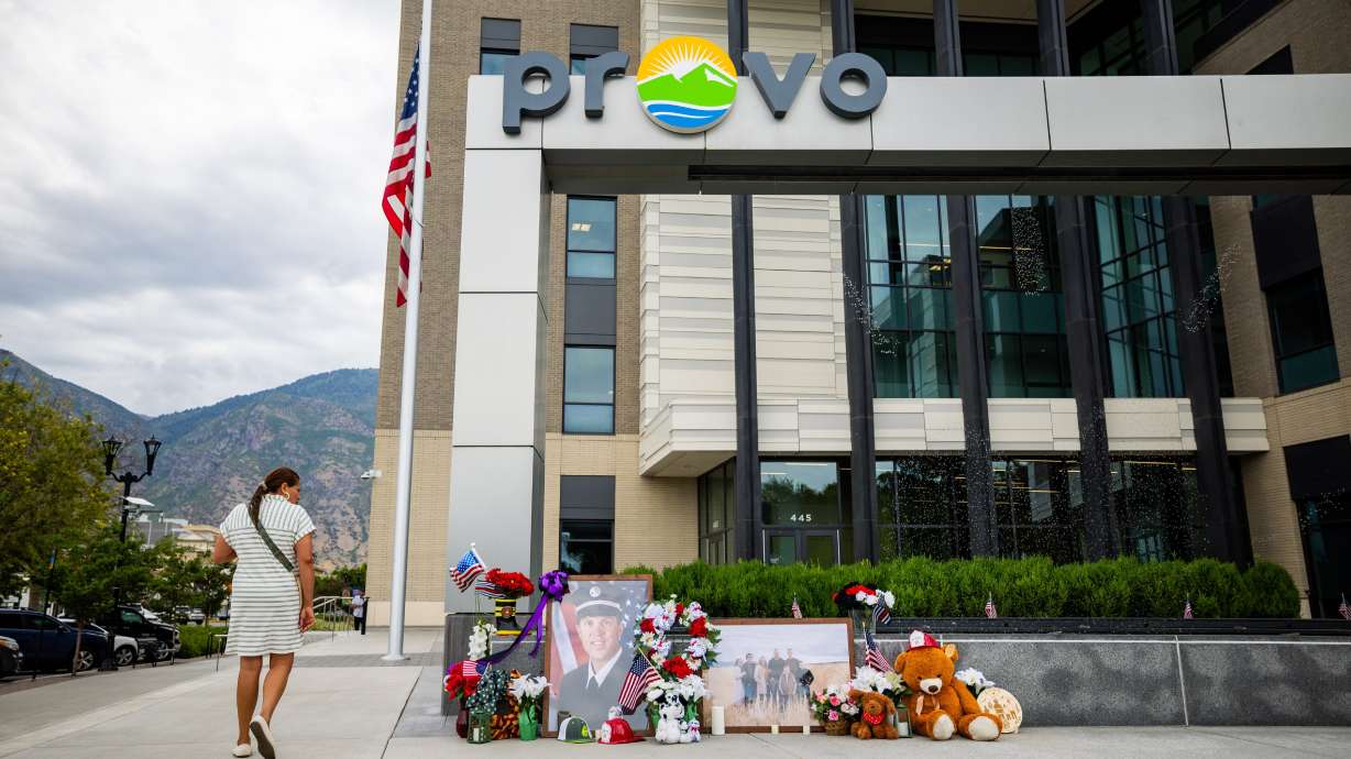 Mery Leiva, from Provo, looks at a memorial with flowers, stuffed animals and photos for Provo Fire Capt. Spencer Long and four members of his family who were killed in a flash flood during a weekend camping and hiking trip in Wayne County, outside of City Hall in Provo on Wednesday.