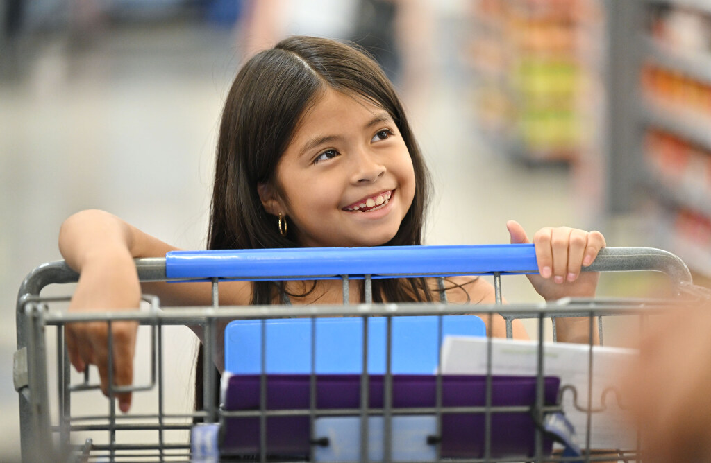 Luna P. smiles at Utah Jazz's Taylor Hendricks as they stand in line at the registers after she and other kids from the Boys & Girls Club of Greater Salt Lake got to shop for back-to-school items at Walmart in West Jordan on July 29, 2025.
