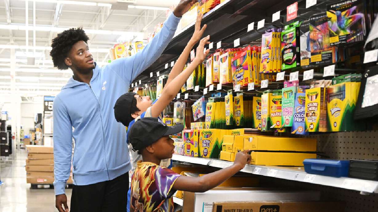 Former Utah Jazz player Taylor Hendricks reaches high on the shelf for some glue sticks for Ryan M. as Scott M. looks at rulers, as they shop for back-to-school items with kids from the Boys & Girls Club of Greater Salt Lake at Walmart in West Jordan.