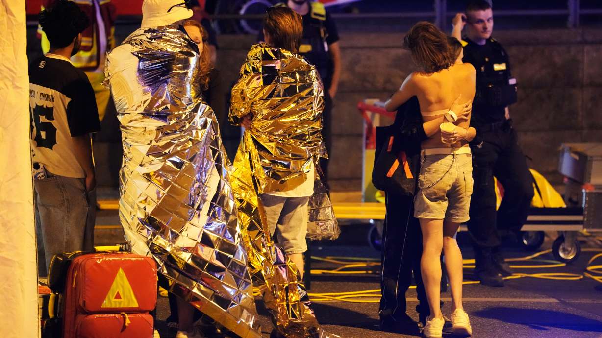 Two people embrace near others wearing thermal blankets as they stand near emergency personnel in Berlin, early Sunday following the cancellation of Christopher Street Day festivities.