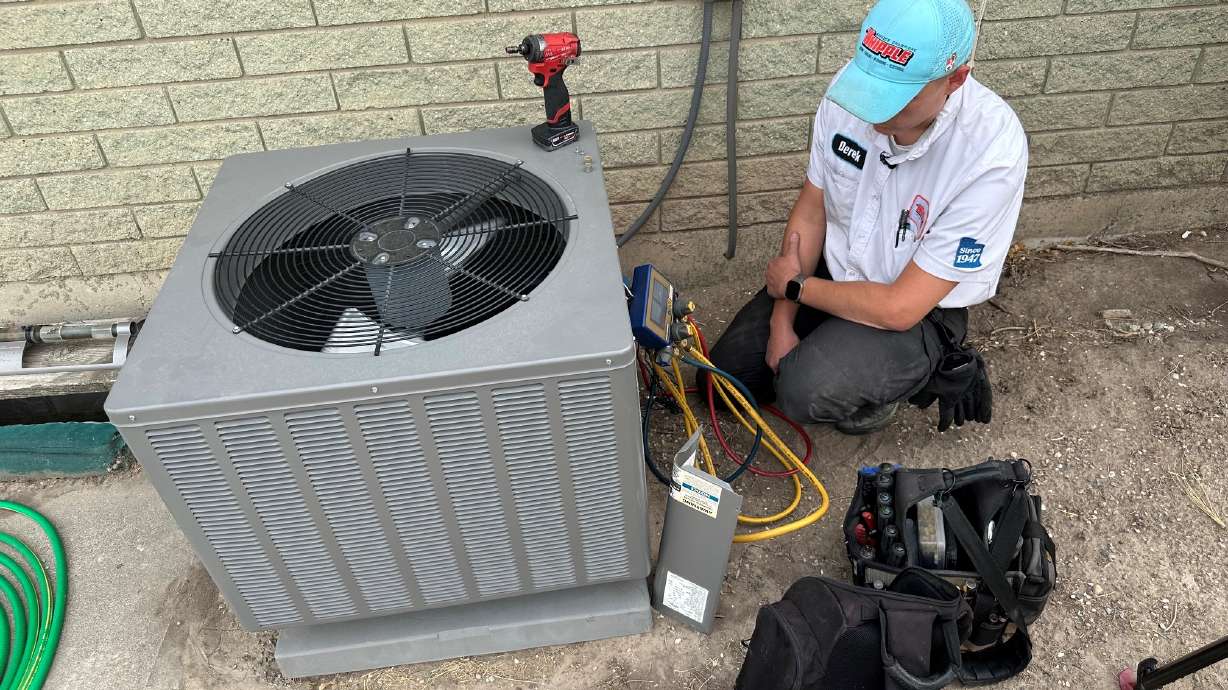 Derek Whipple, a HVAC service technician, works on an AC unit at a home in Taylorsville. HVAC technicians in Utah are working overtime to keep up with demand.