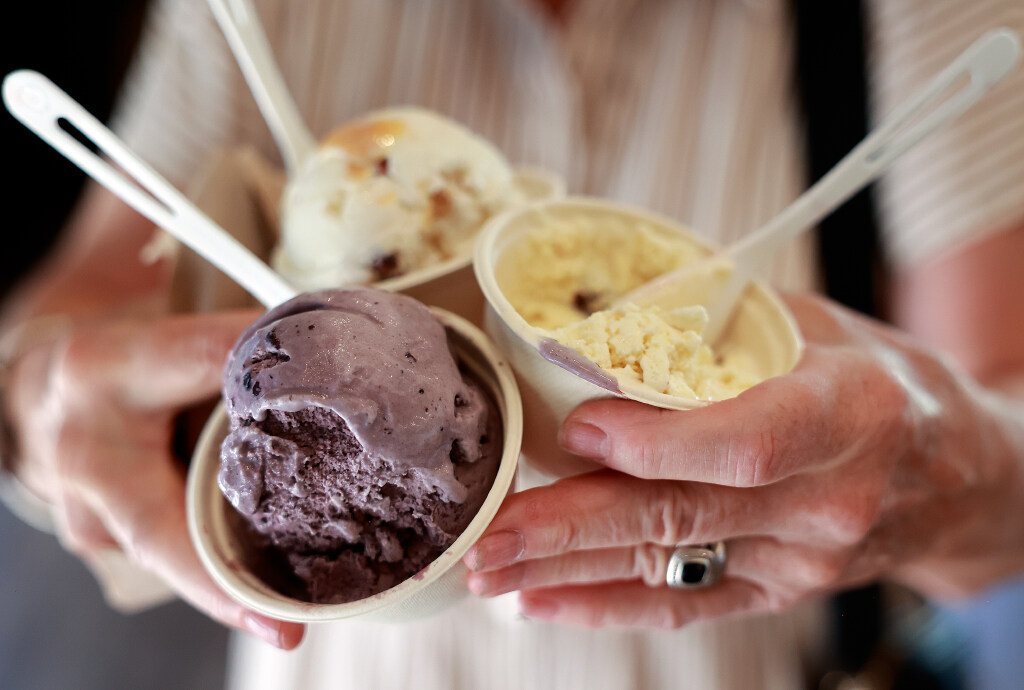 A woman holds three cups of ice cream, including I’m Your Huckleberry, Coconut Castaway and Monkey Business flavors, at The Creamery in Beaver on Thursday, July 9, 2026.