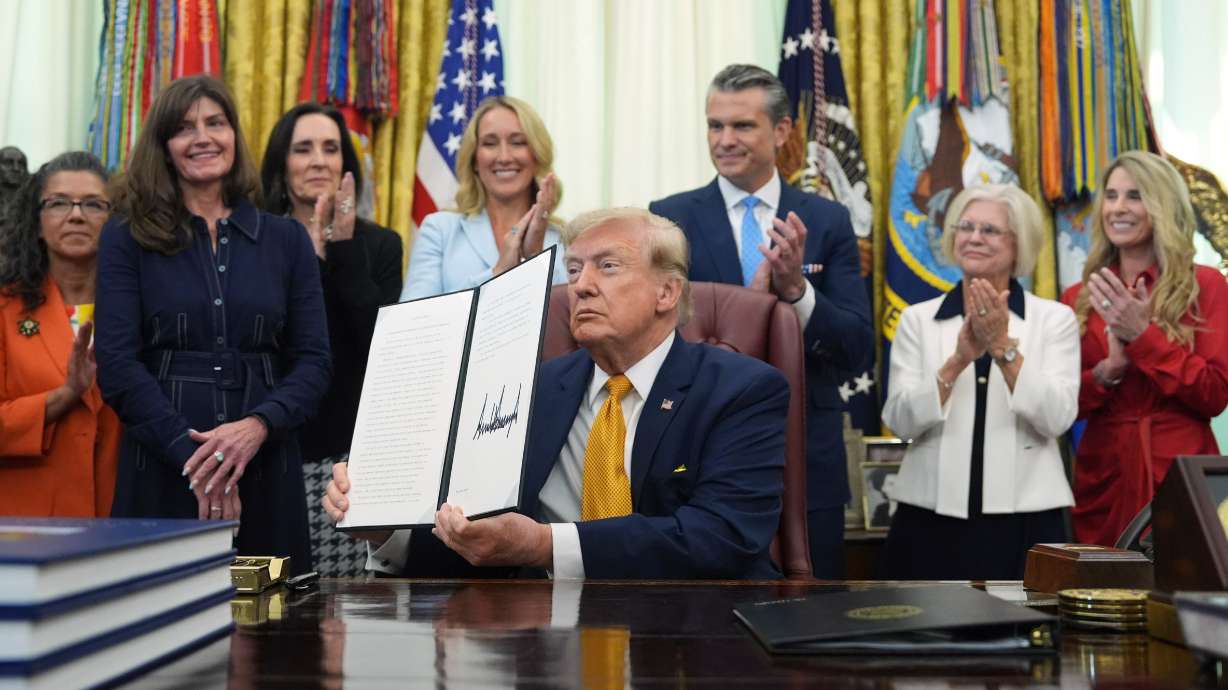 President Donald Trump holds a signed executive order as Jennifer Hegseth, Defense Secretary Pete Hegseth and guests look on during a meeting about military families in the Oval Office of the White House, Monday in Washington.