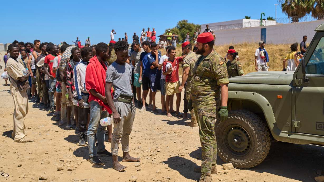 Migrants who crossed into Spain from Morocco line up for water distributed by Spanish soldiers in the Spanish enclave of Ceuta, Sunday, Aug. 2, 2026.
