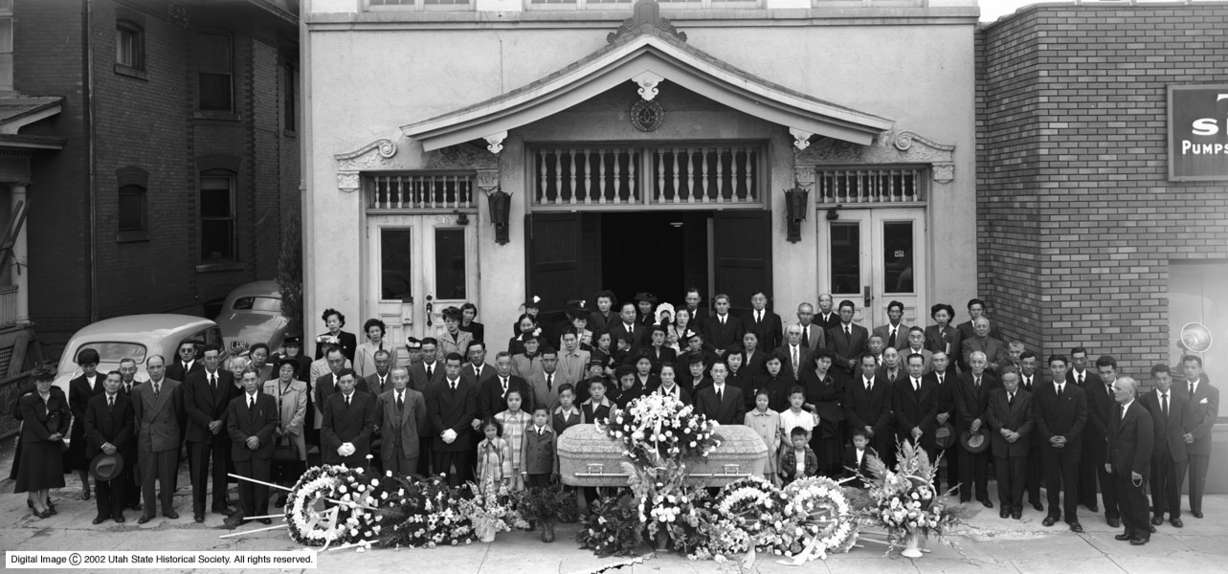 The funeral in May of 1949 outside the original Salt Lake Buddhist Temple was being held to honor the death of Mr. Sajiro Shibuya. It was officiated by Mrs. Terakawa, wife of the Reverend Chonen Terakawa. This photo was identified by Mr. Thomas M. Endo (Shibuya's grandson), who is pictured to the left of the casket in the image, with his sisters, Alice and Xan.