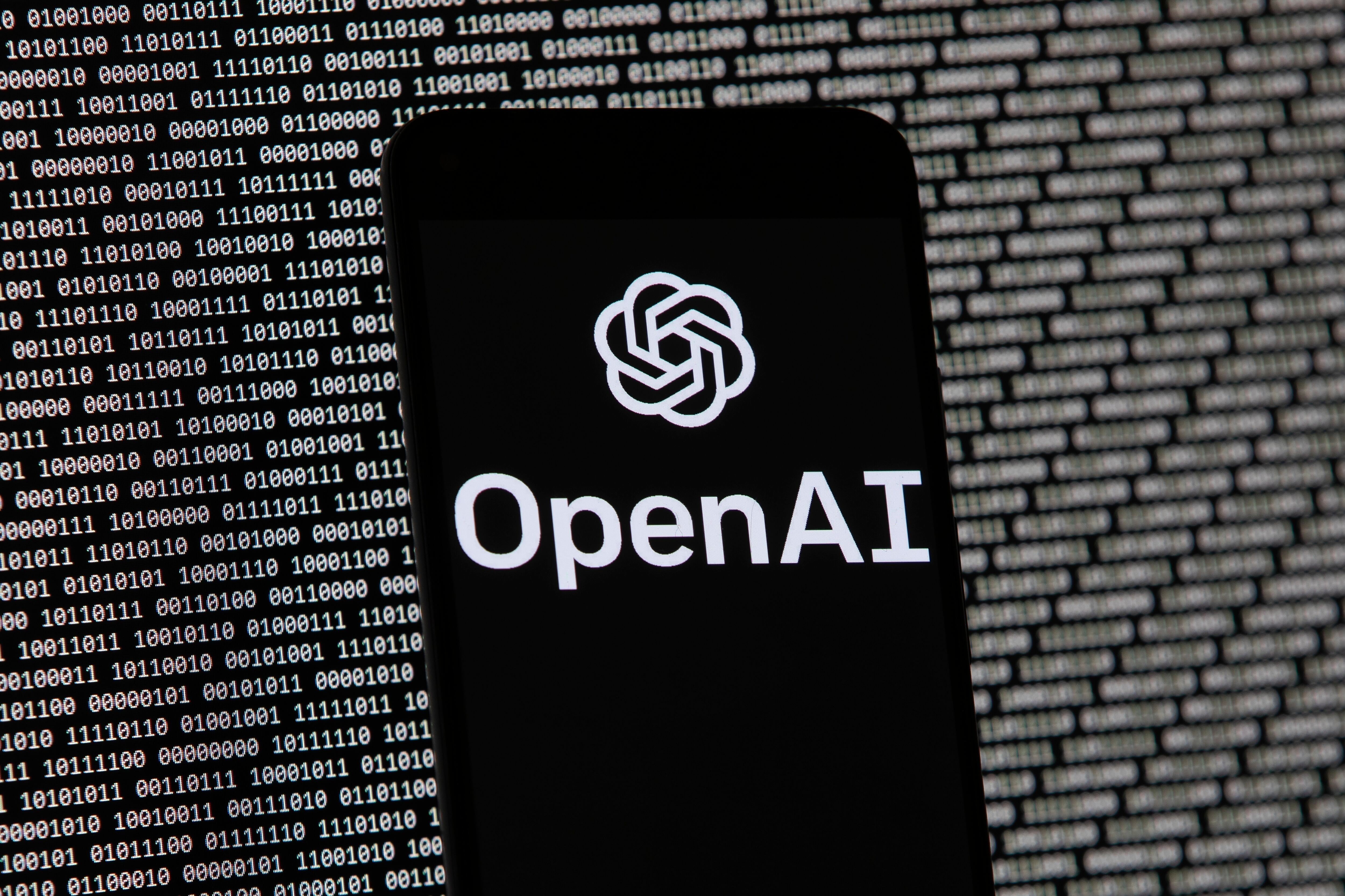 The OpenAI logo appears on a mobile phone in front of a computer screen with random binary data, March 9, 2023, in Boston. Rep. Celeste Maloy introduced an AI regulatory bill of her recently.