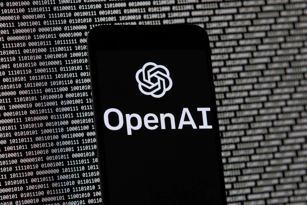 The OpenAI logo appears on a mobile phone in front of a computer screen with random binary data, March 9, 2023, in Boston. Rep. Celeste Maloy introduced an AI regulatory bill of her recently.