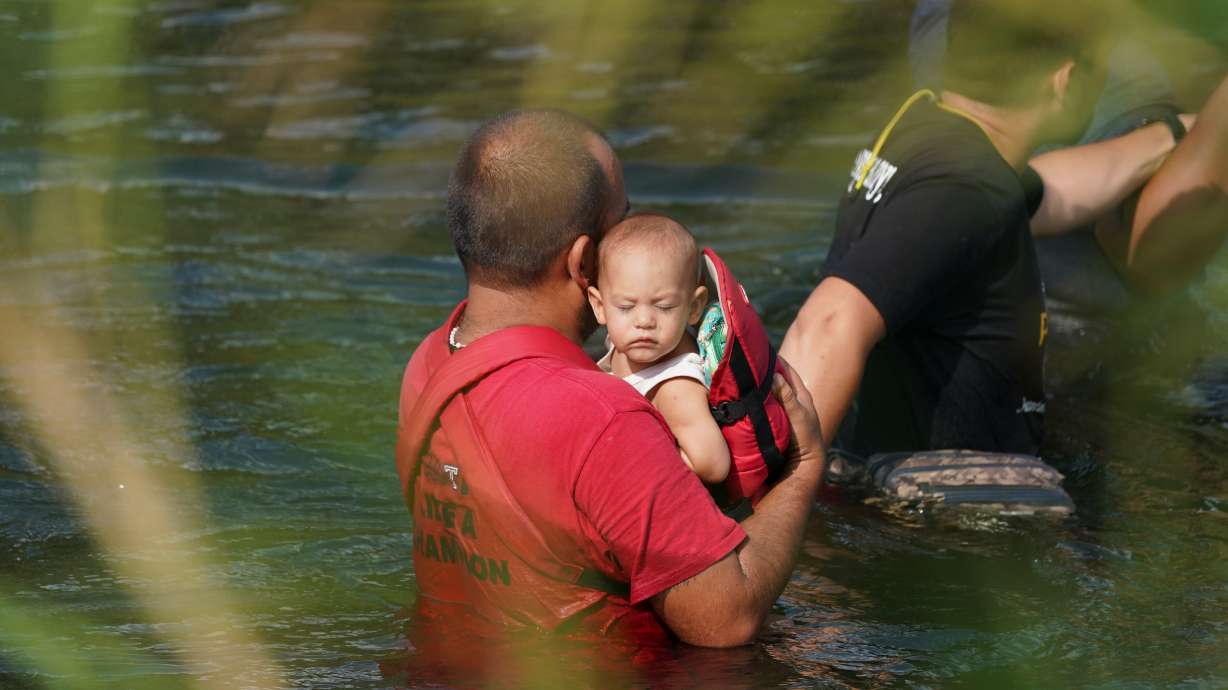 A migrant crosses the Rio Grande river with a child in arms, as seen from Matamoros, Mexico, May 10, 2023. Utah Sen. Mike Lee is seeking ways to close what he views as loopholes in federal immigration law that allow adults to take advantage of children in order to enter the United States illegally.