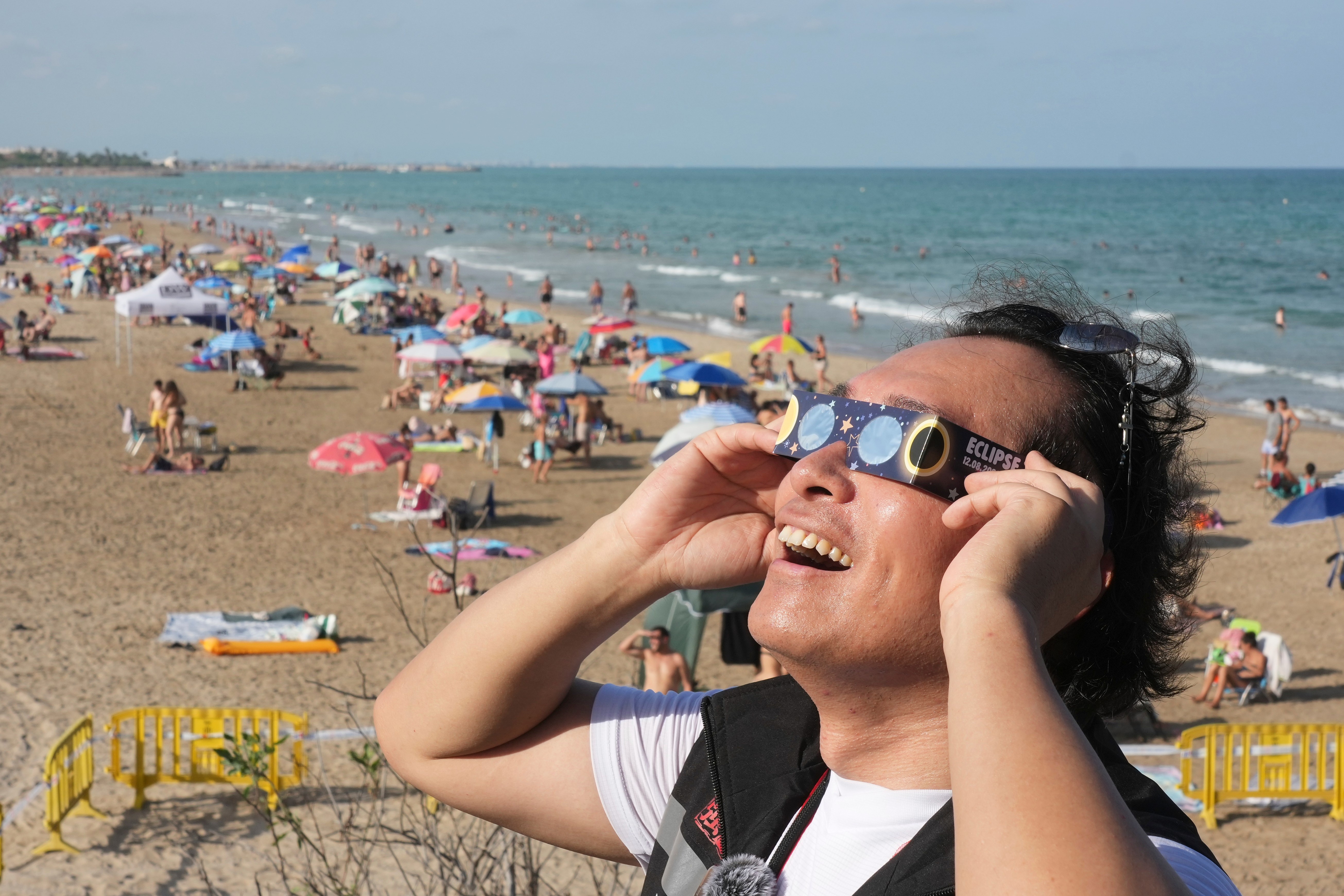 A man wears special eclipse glasses, as beachgoers gather before a total solar eclipse set to begin around sunset, at a beach near Valencia, Spain, Wednesday. Eclipse glasses like these went fast.