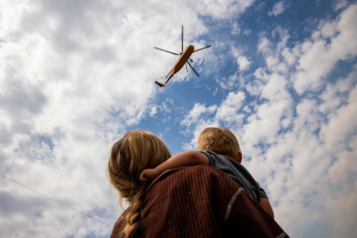 Sisalee Richins Beddoes and son Gus watch a firefighting helicopter travel to refill its bucket in a pool full of water in Henefer to fight the Rocky Canyon Fire on Tuesday. This year's fire season has already cost Utah millions in resources.