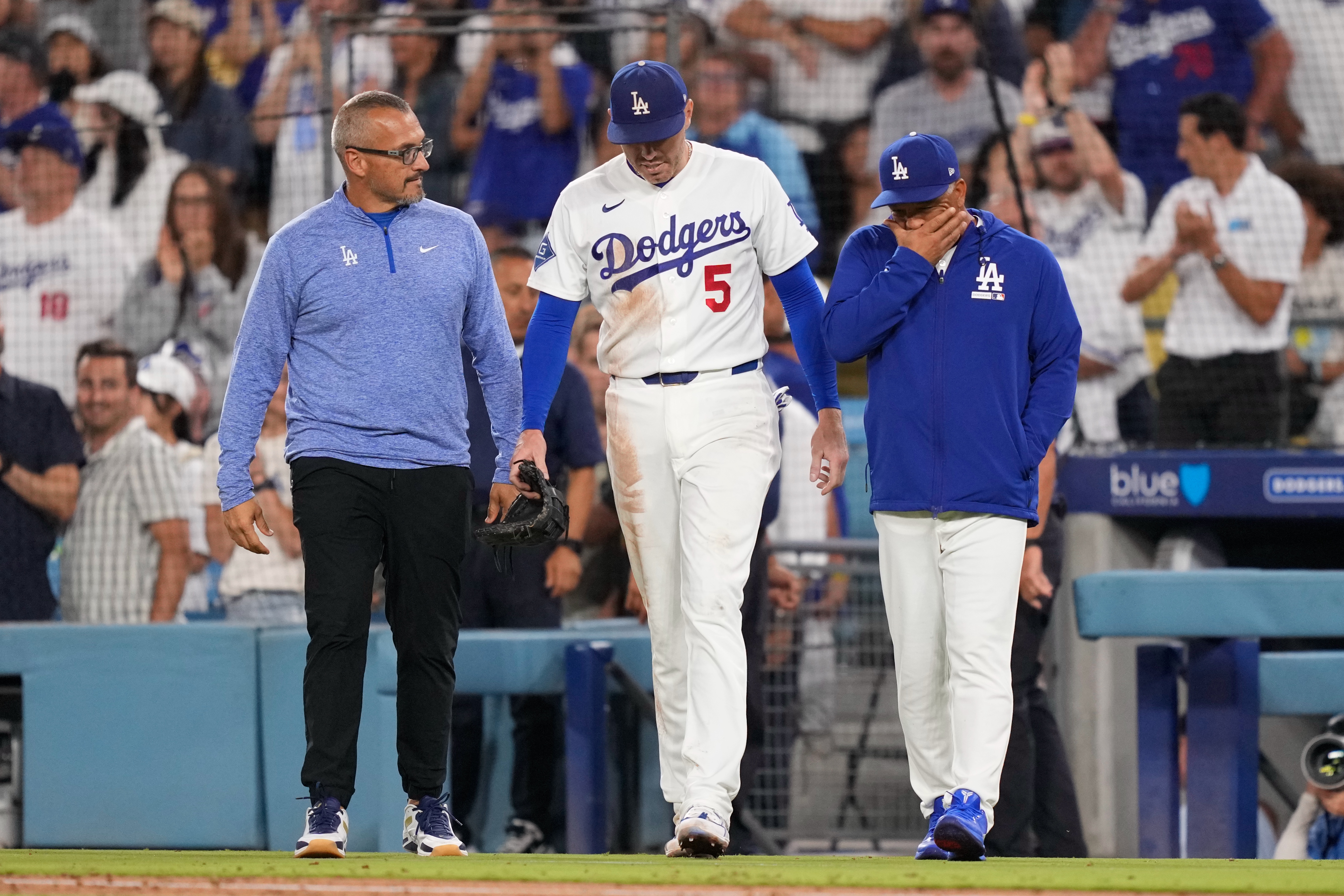 Los Angeles Dodgers first baseman Freddie Freeman, center, walks back on to the field accompanied by manager Dave Roberts, right, and trainer Greg Barajas after he fell into the dugout while trying to catch a foul ball hit by Kansas City Royals' Isaac Collins during the eighth inning of a baseball game Wednesday, Aug. 12, 2026, in Los Angeles. 