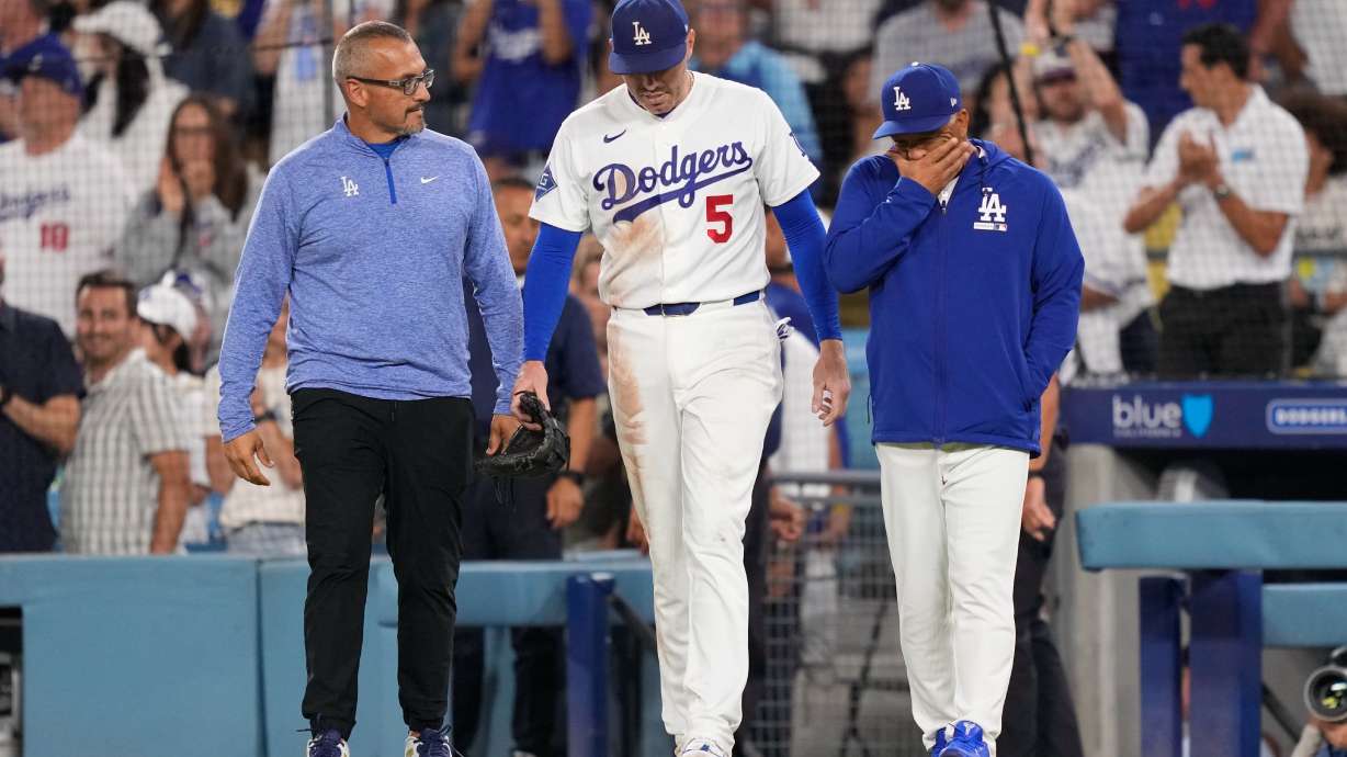 Los Angeles Dodgers first baseman Freddie Freeman, center, walks back on to the field accompanied by manager Dave Roberts, right, and trainer Greg Barajas after he fell into the dugout while trying to catch a foul ball hit by Kansas City Royals' Isaac Collins during the eighth inning of a baseball game Wednesday, Aug. 12, 2026, in Los Angeles.