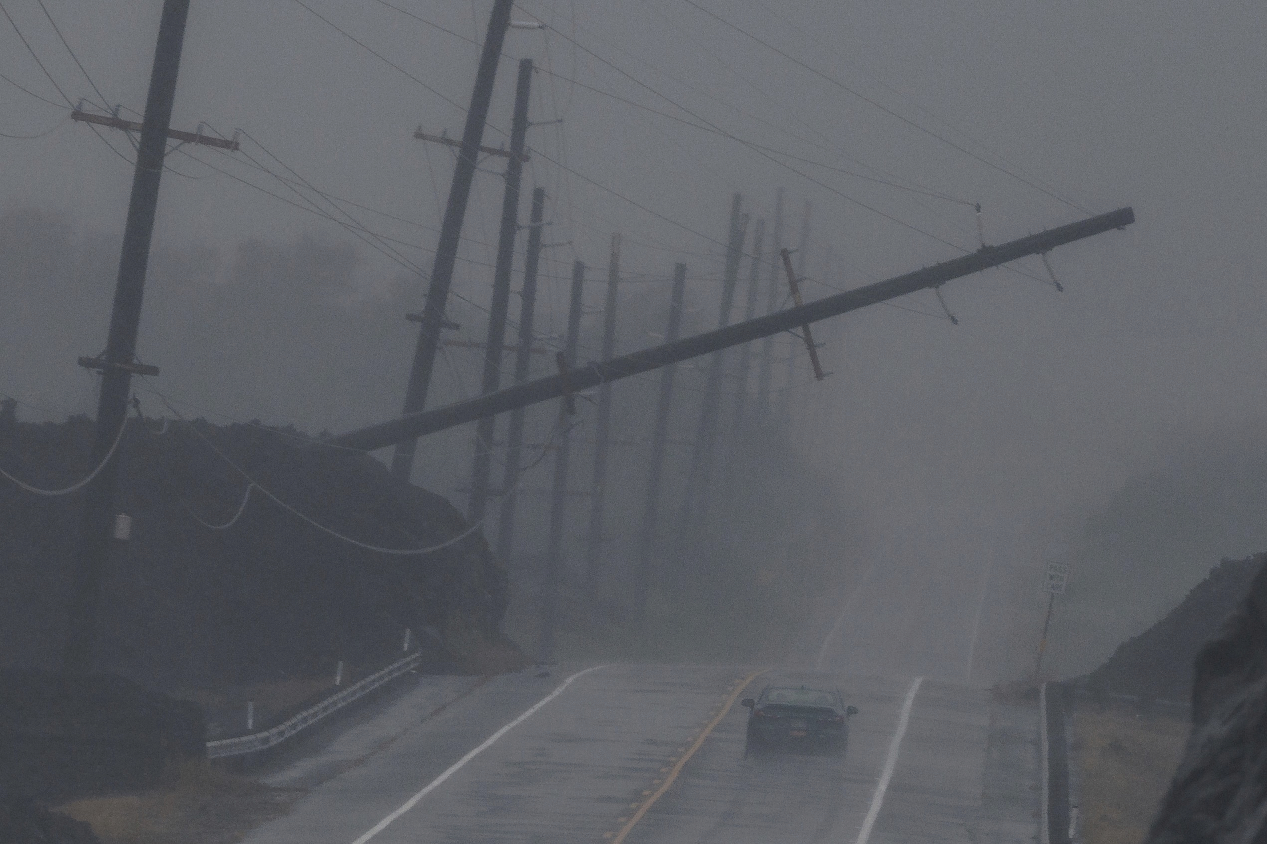 A vehicle drives near a downed utility pole dangling above Mamalahoa Highway during Hurricane Lala near Ocean View, Hawaii, Saturday.