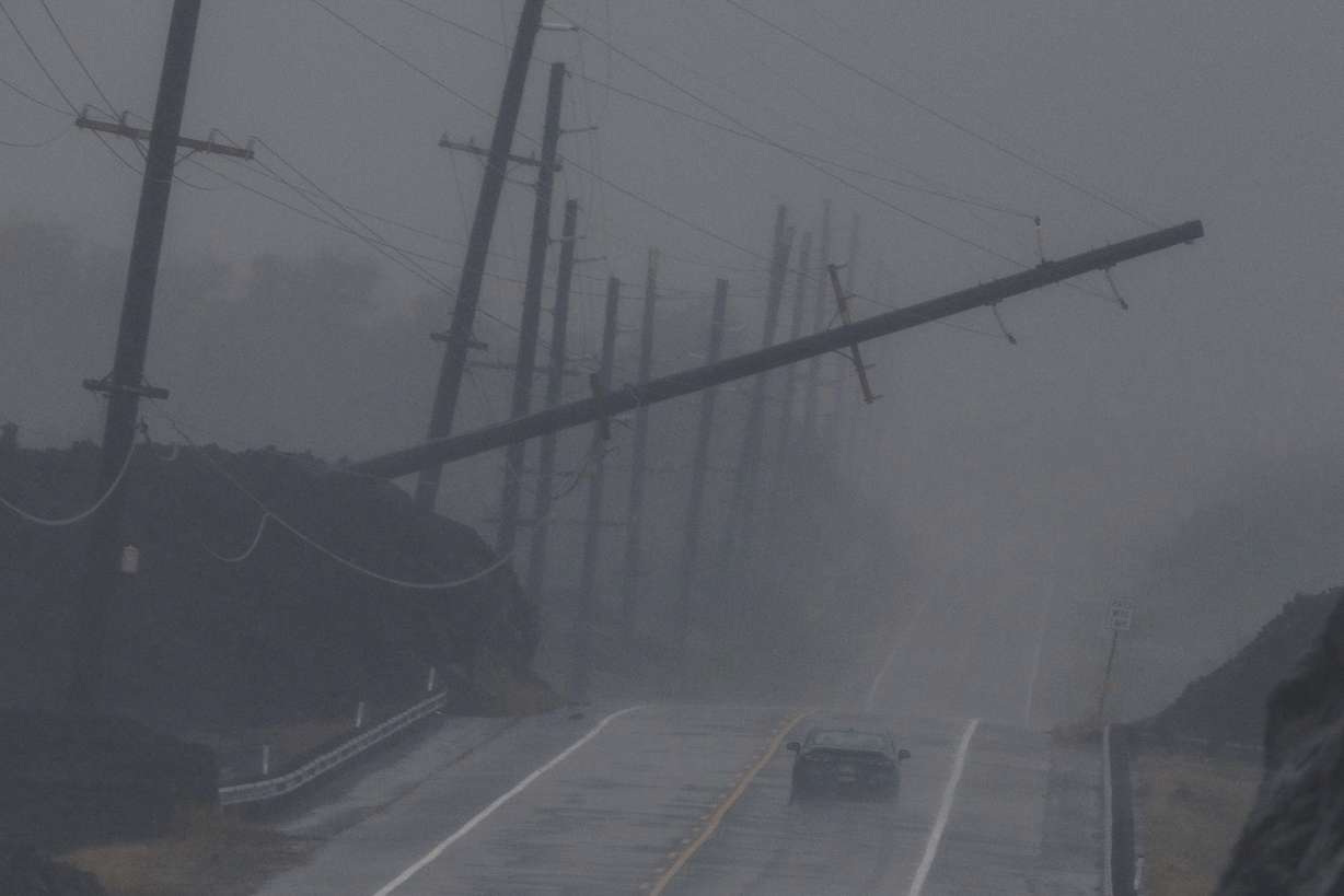 A vehicle drives near a downed utility pole dangling above Mamalahoa Highway during Hurricane Lala near Ocean View, Hawaii, Saturday.
