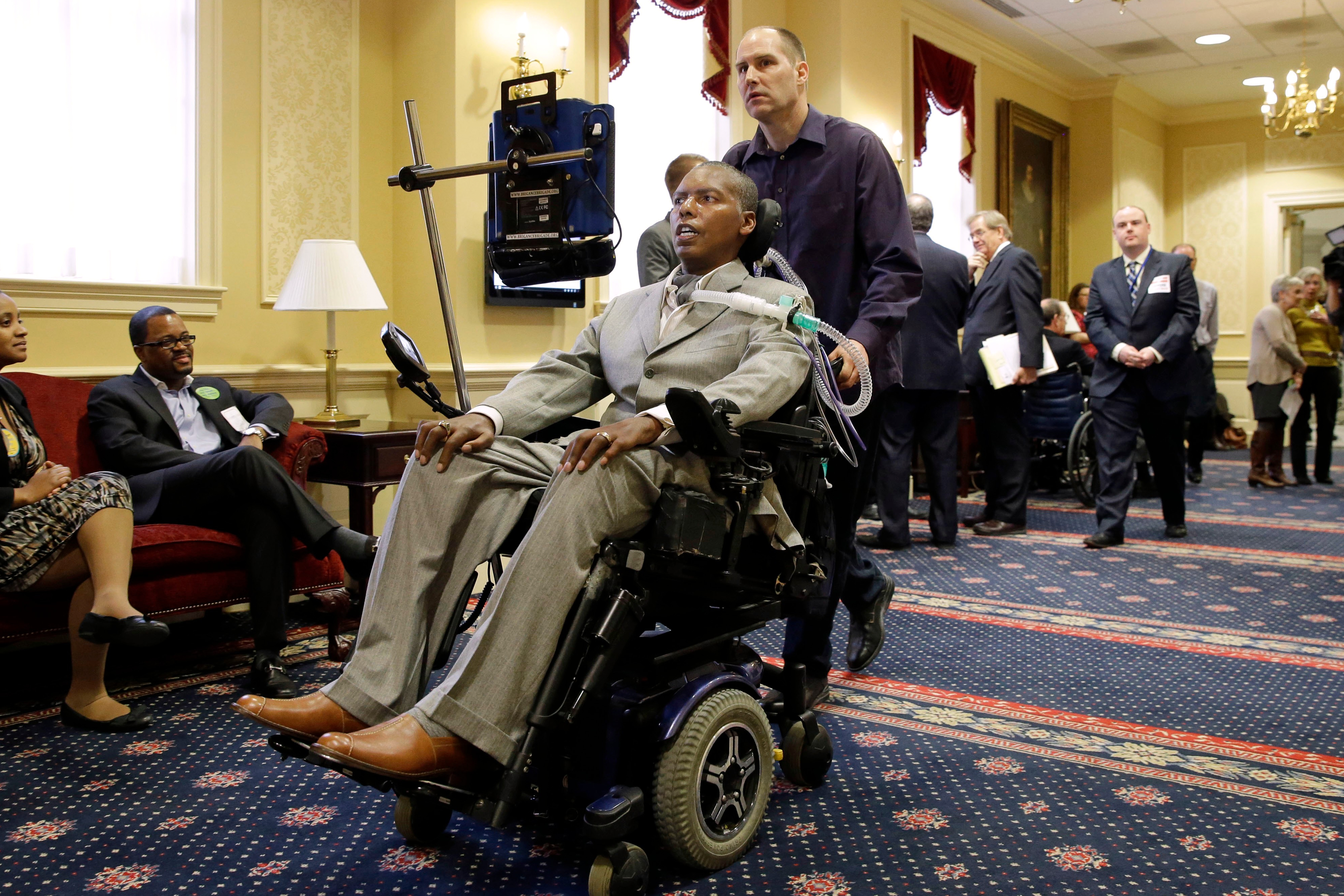 FILE - Former Baltimore Ravens NFL football player O.J. Brigance, center, current senior advisor to player development, is pushed by a nurse outside of a committee room in Annapolis, Md., March 10, 2015, after testifying to Maryland lawmakers against a right-to-die bill. 