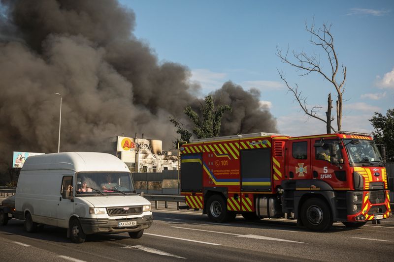 A firetruck and other vehicles pass by a warehouse hit by a Russian drone strike with a melted Avrora Multimarket sign, amid Russia's attack on Ukraine, in Kyiv region, Ukraine, Monday,