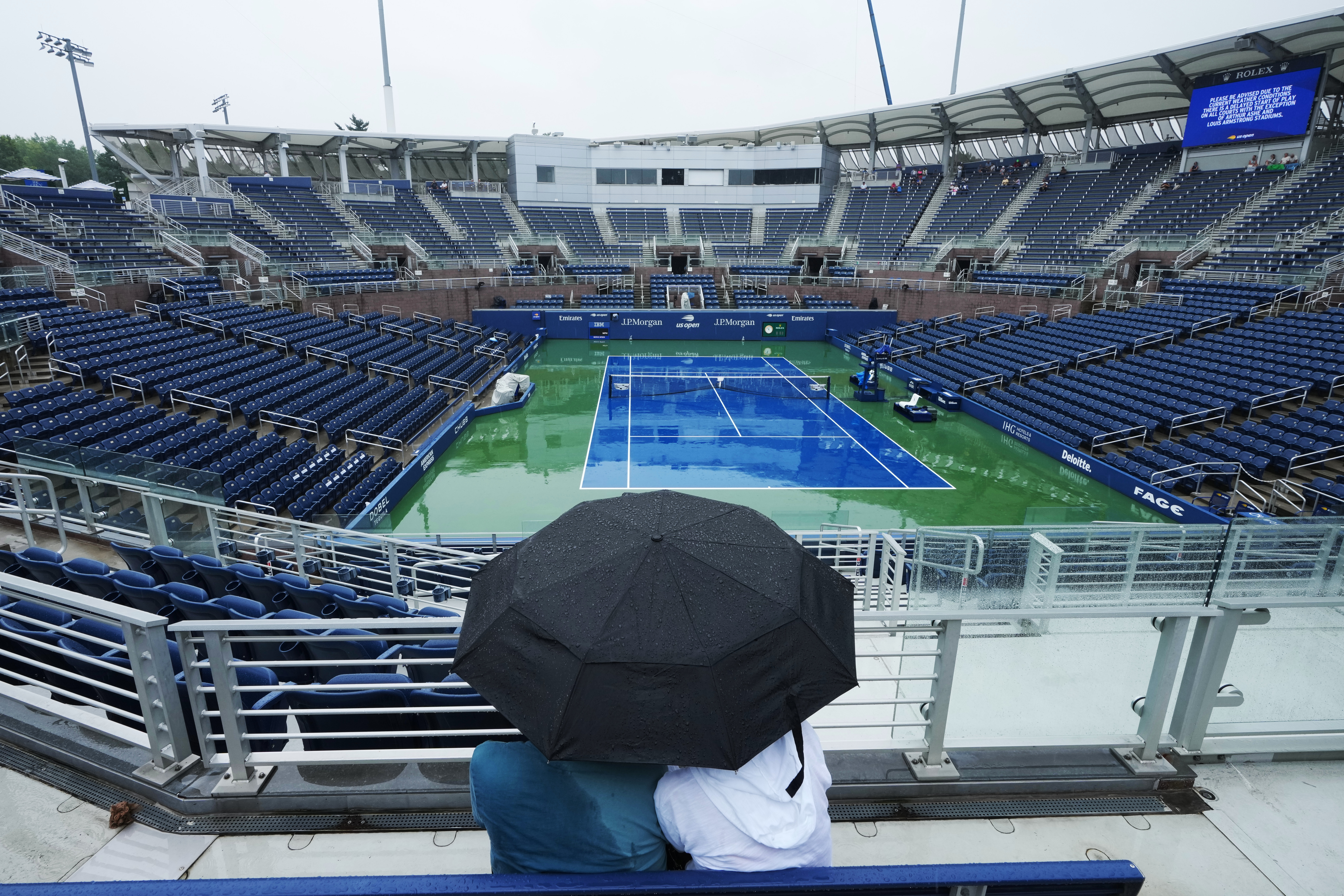 A couple sits under an umbrella during a rain delay on the Grandstand court during the first round of the U.S. Open tennis championships Tuesday, Sept. 1, 2026, in New York.