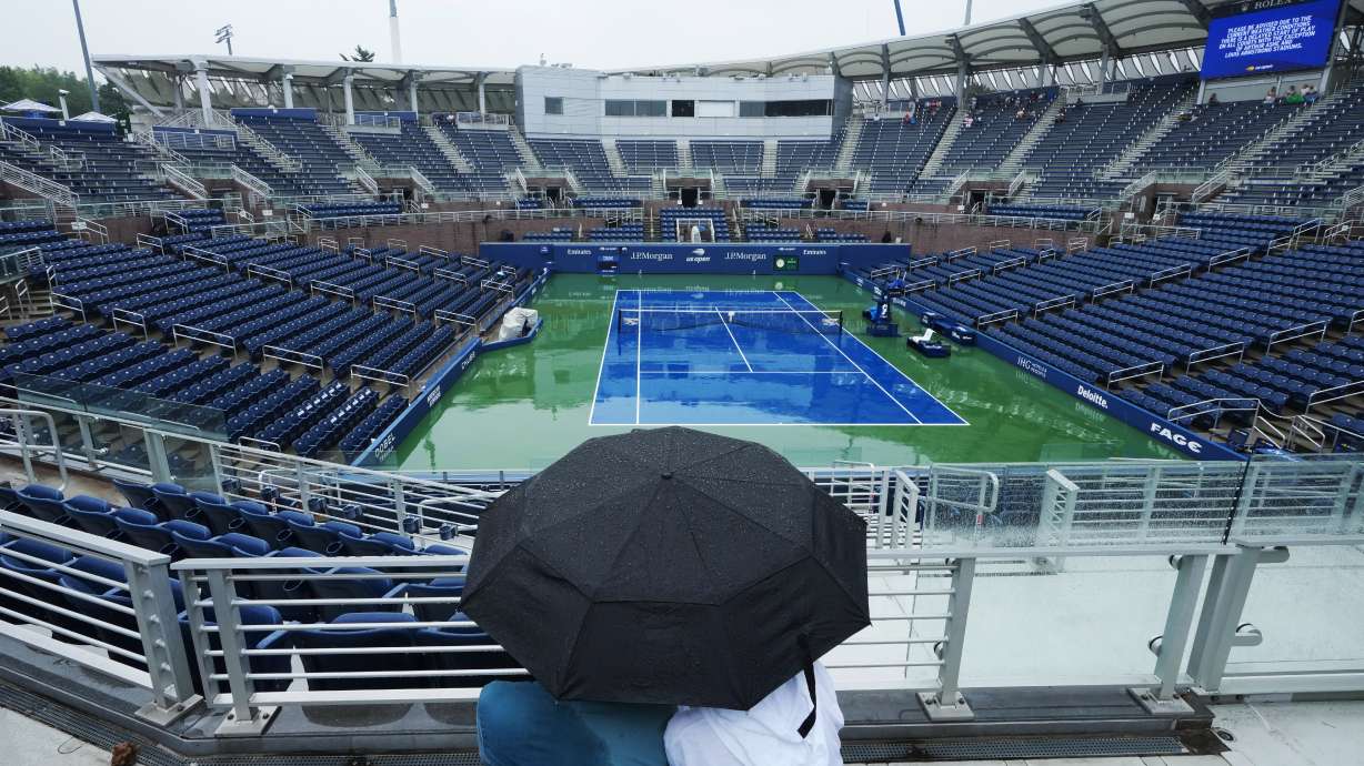 A couple sits under an umbrella during a rain delay on the Grandstand court during the first round of the U.S. Open tennis championships Tuesday, Sept. 1, 2026, in New York.
