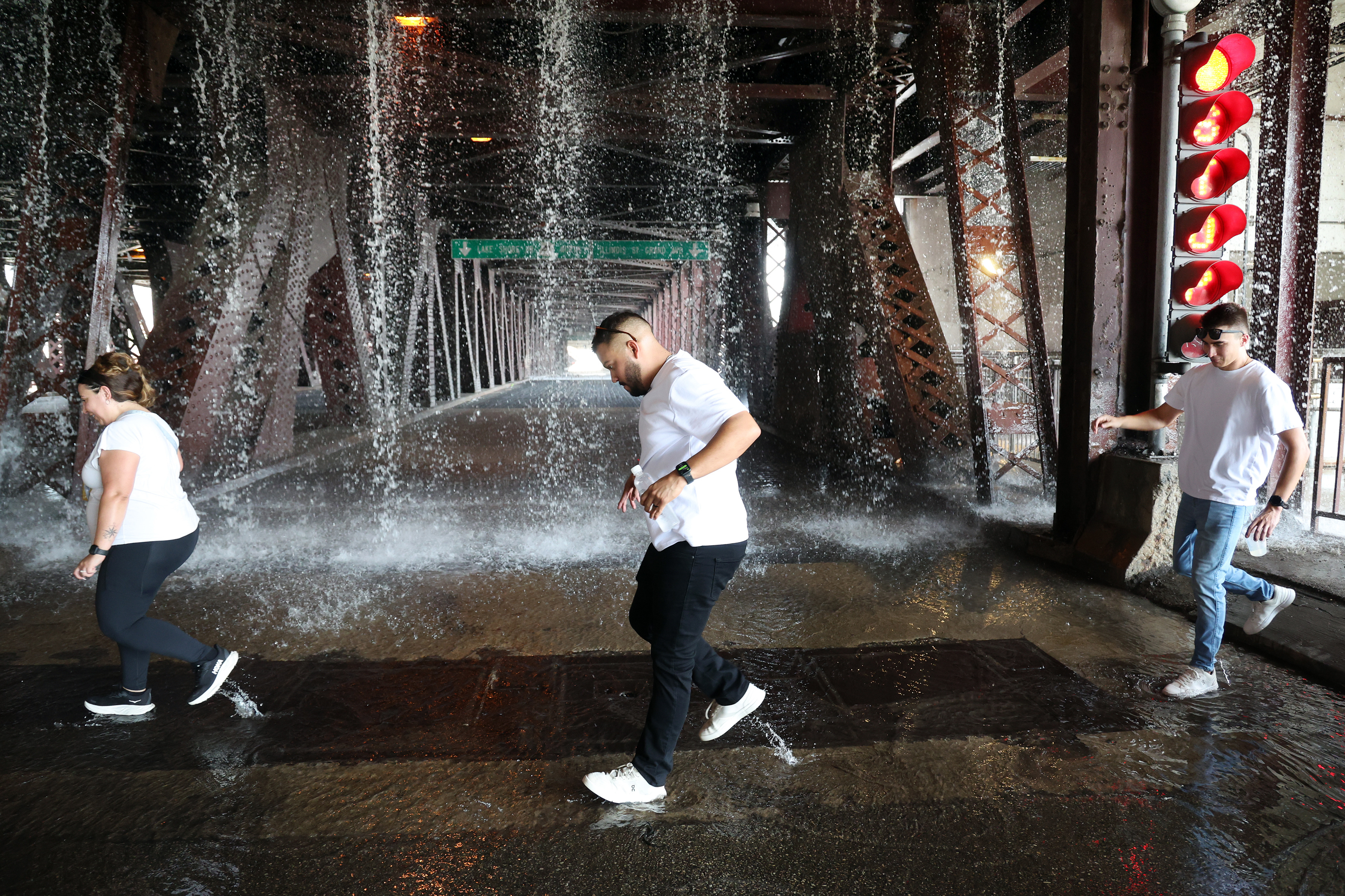 People scamper west across the lower level of the DuSable Lake Shore Drive bridge over the Chicago River on Wednesday, Sept. 2, 2026, as water pumped by a Chicago Fire Department boat flows down onto the double-leaf, double-deck, fixed counterweight bridge. 