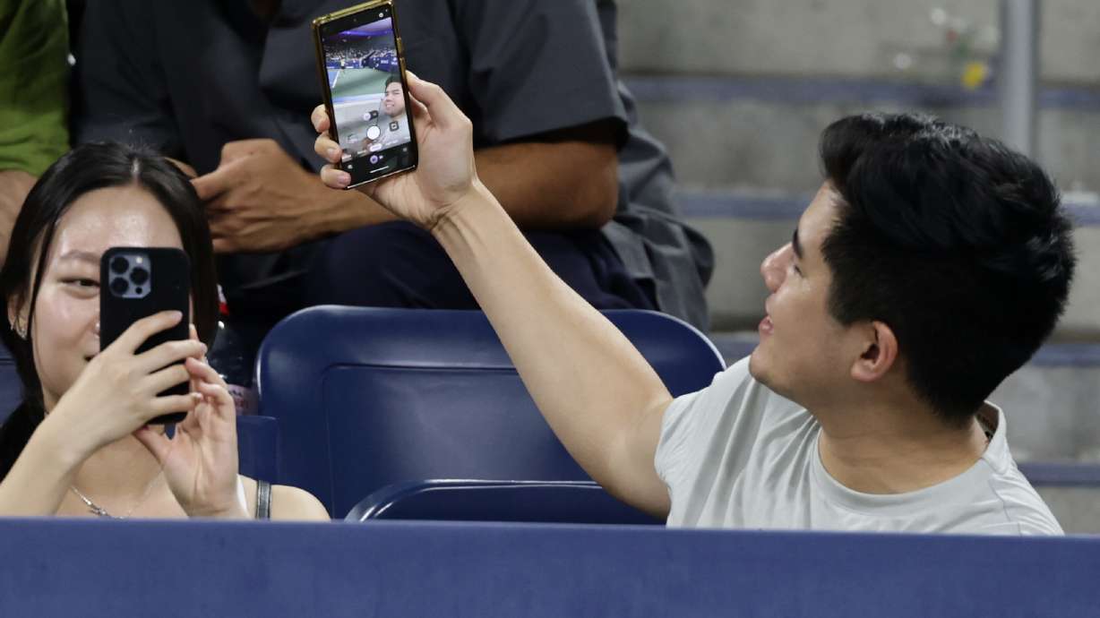 A fan takes a selfie as Elena Rybakina, of Kazakhstan, serves to Jessica Bouzas Maneiro, of Spain, during the second round of the U.S. Open tennis championships, Thursday, Sept. 3, 2026, in New York.