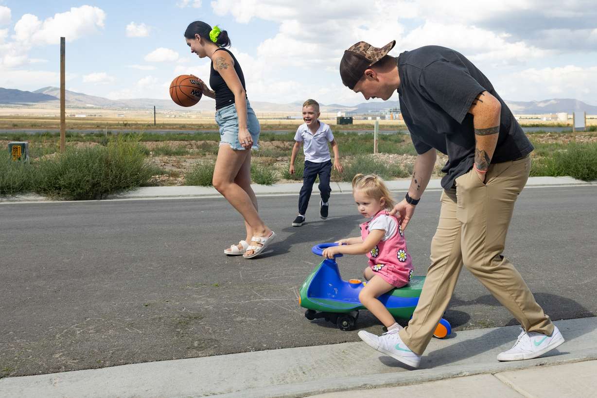Austin Campbell pushes his daughter Piper on her tricycle while his wife, Jessi, plays basketball with their son Quinn near their home in Eagle Mountain on Tuesday. Austin Campbell recently was laid off from his job.
