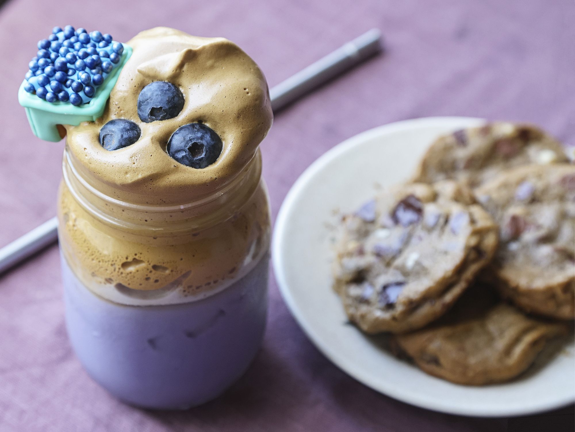 Blueberry Dalgona Coffee recipe, prepared by Lauren J. Mapp at her home in San Diego, CA, in April 2021. Topped with blueberries and adorned with a Mug Buddy Cookie (left) and Chocolate Chip Cookies (right).