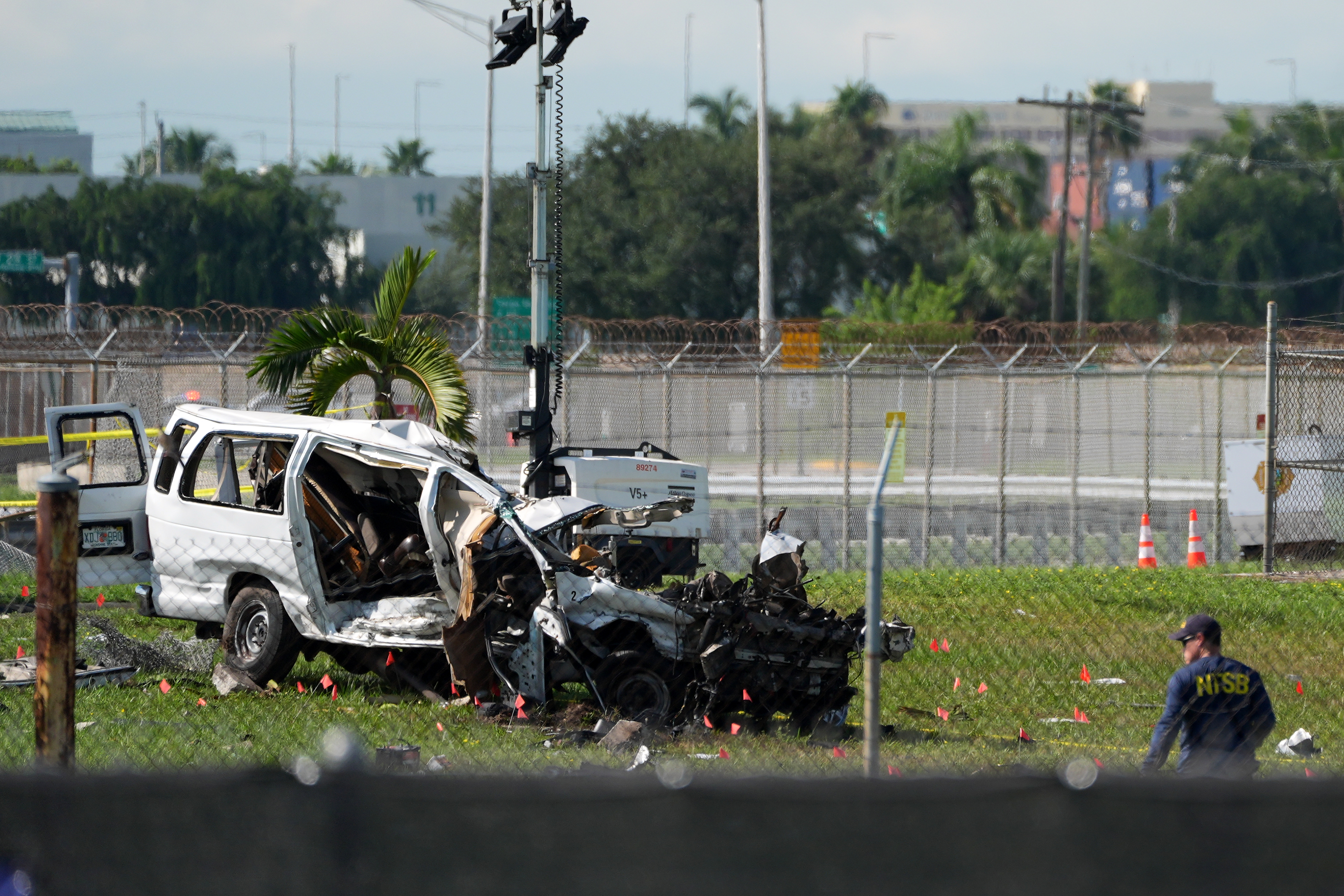 An NTSB investigator works near a damaged van at the site where an Amazon cargo plane overshot the runway two days earlier while landing at Miami International Airport, Tuesday. The five people killed in the crash were inside a van used by plane cleaners, authorities said.