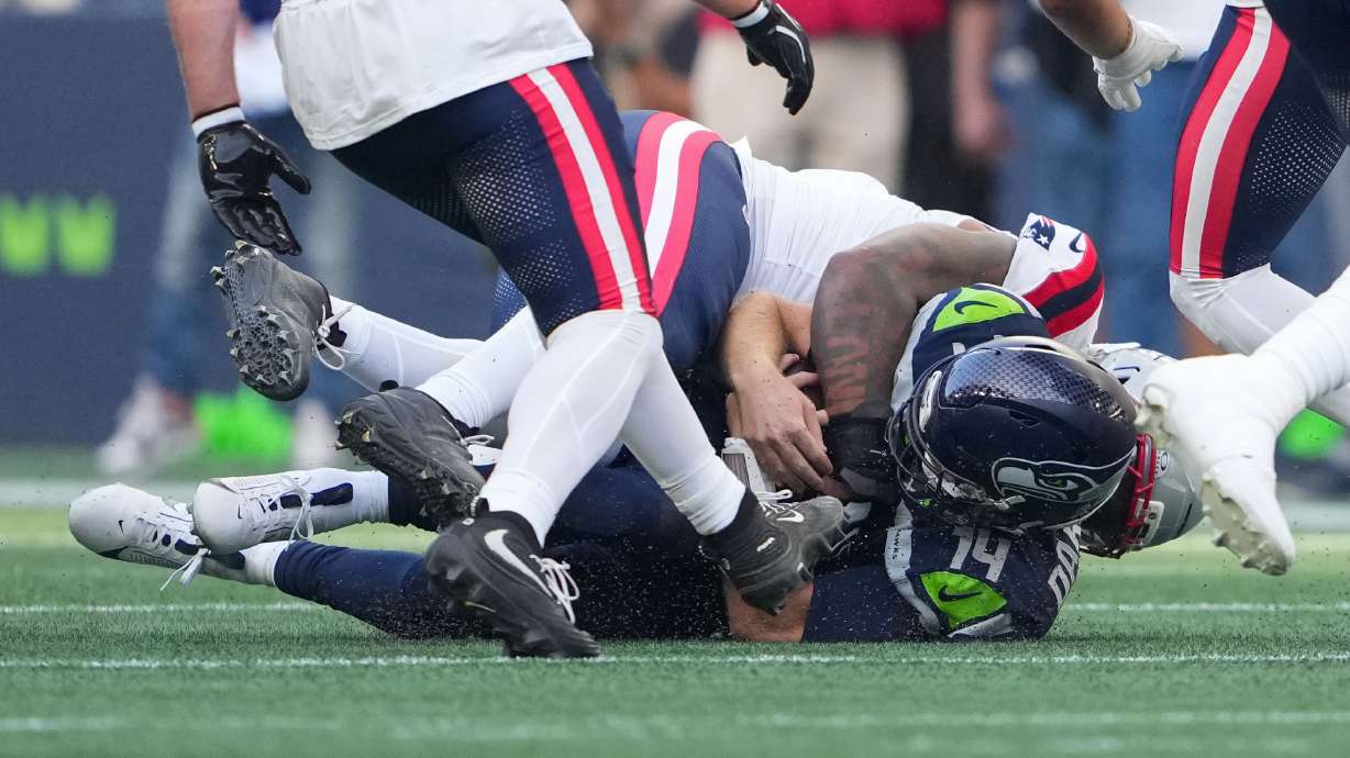Seattle Seahawks quarterback Sam Darnold, (14) is sacked by New England Patriots linebacker Dre'mont Jones, behind, during the first half an NFL football game, Wednesday, Sept. 9, 2026, in Seattle.
