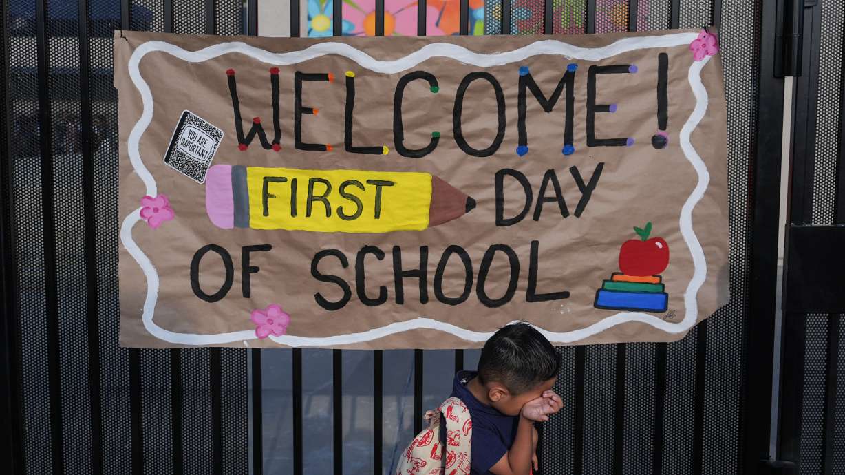 A student wipes his face while his mother takes a photo of him with a sign on the first day of school at Betsy Ross Elementary School in Anaheim, Calif., on Aug. 6.