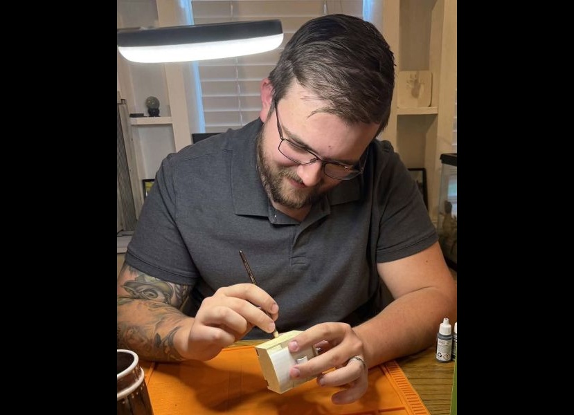 Jonah Saunders carefully paints the intricate details on one of his miniature creations. Saunders combines his skills in design, 3D modeling and painting to recreate local landmarks and other meaningful buildings.