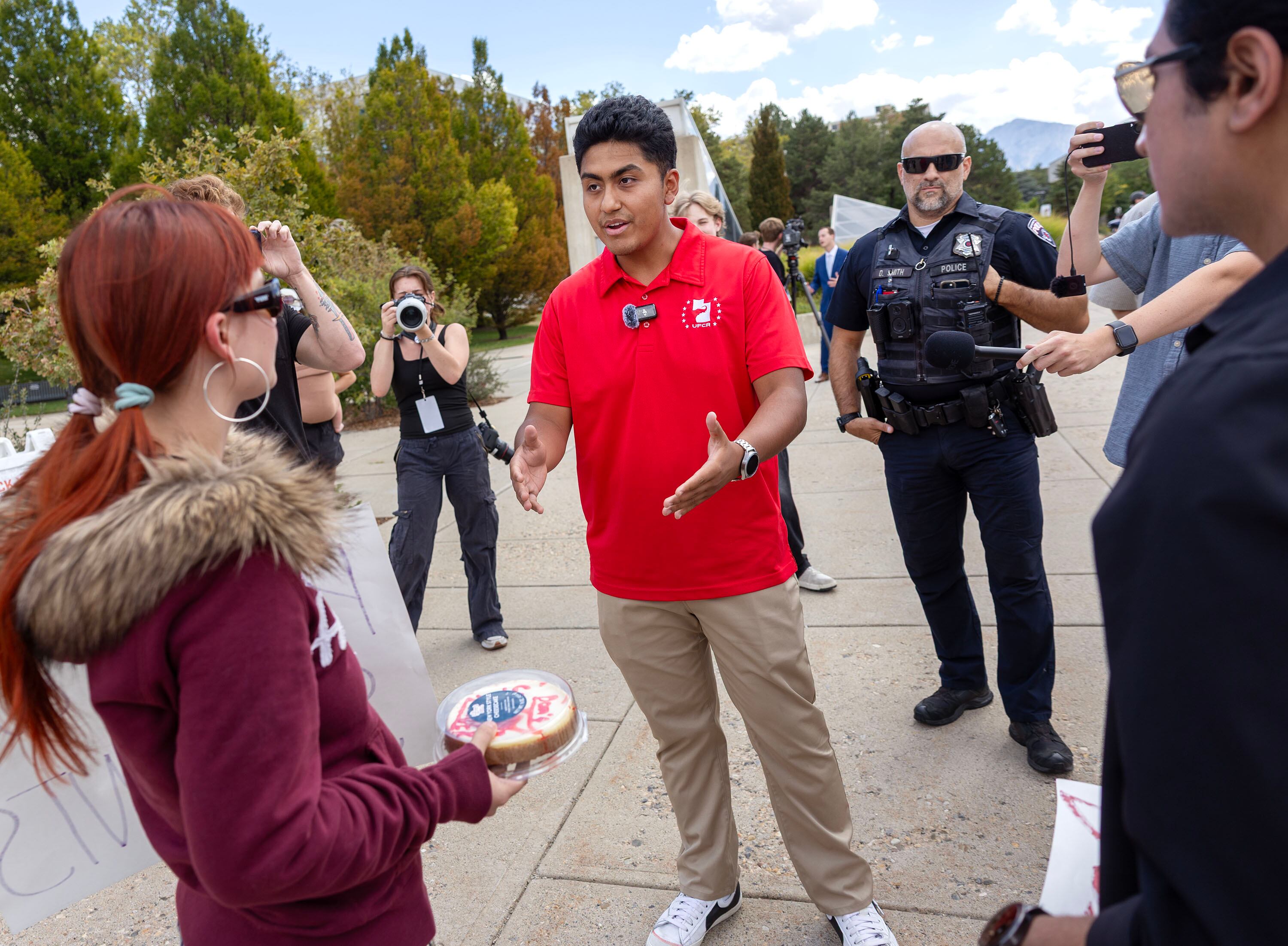 Daylan Alzamora, president of the University of Utah College Republicans chapter, offers a cake to Lili Nilsson, who is protesting on the University of Utah campus on Wednesday. A University of Utah student has apologized after facing intense online backlash over a photo showing the student posing with a cake bearing the words “Happy Kirkiversary,” a reference to last week’s one-year anniversary of Charlie Kirk’s death.