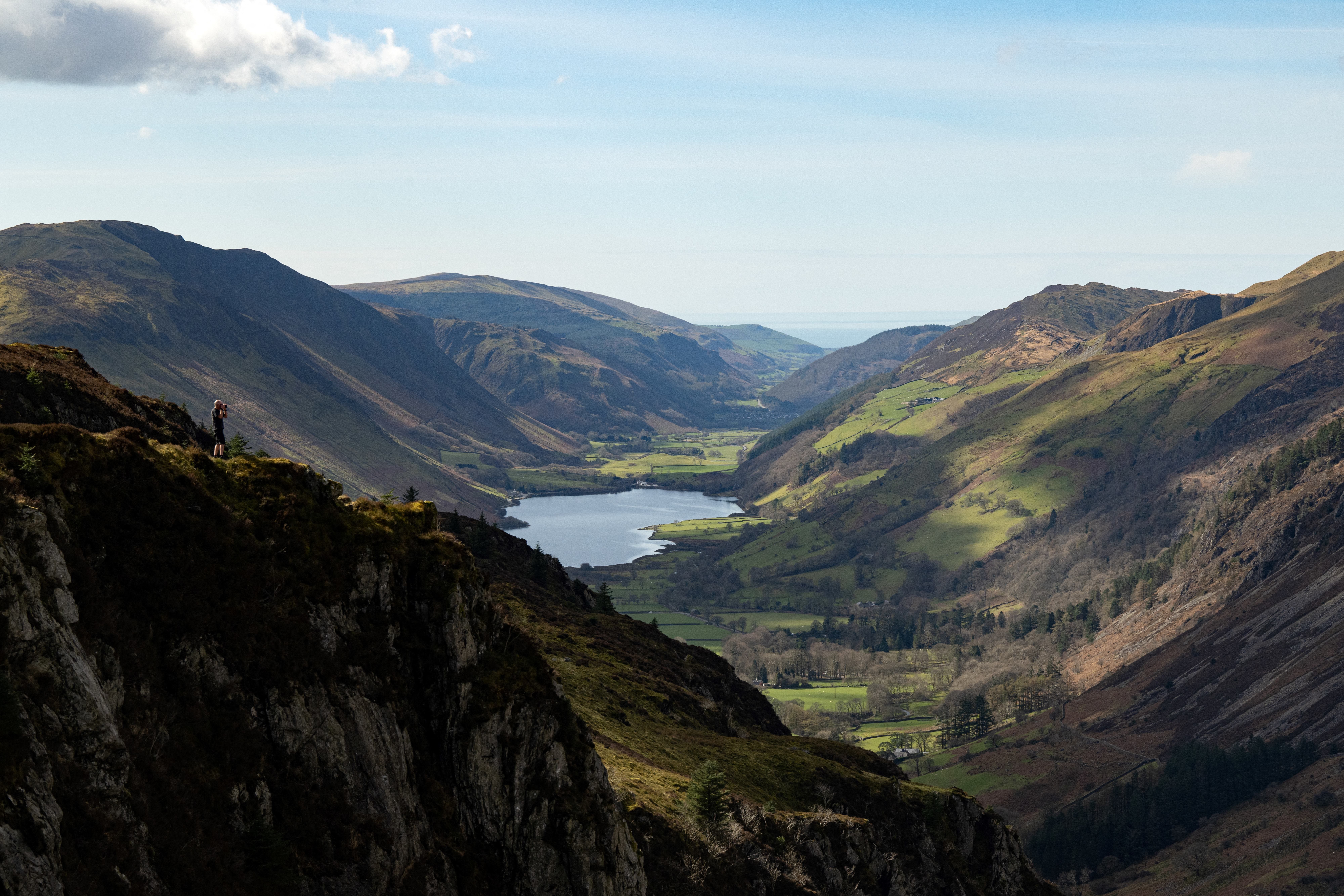 A hiker stands on a cliff top overlooking Tal-y-llyn Lake in Snowdonia National Park, north Wales in 2023.