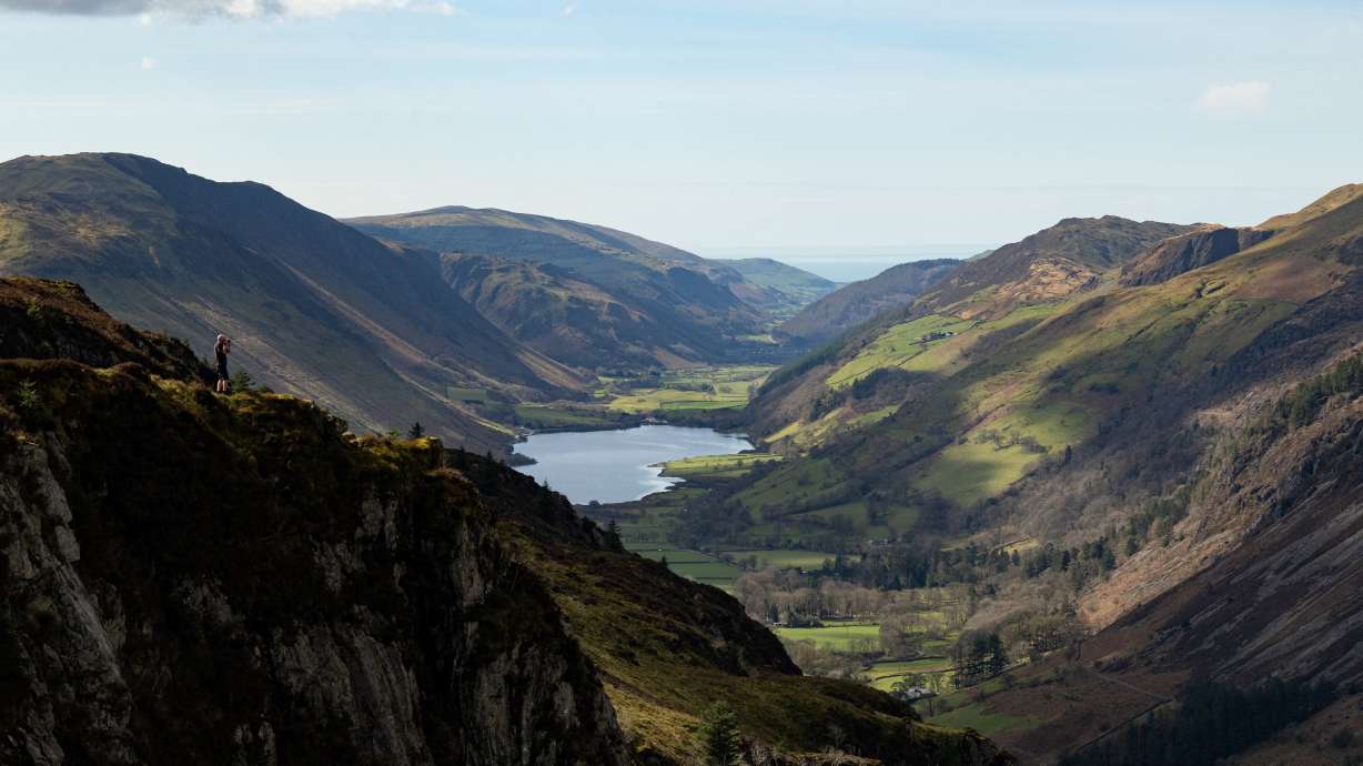 A hiker stands on a cliff top overlooking Tal-y-llyn Lake in Snowdonia National Park, north Wales in 2023.