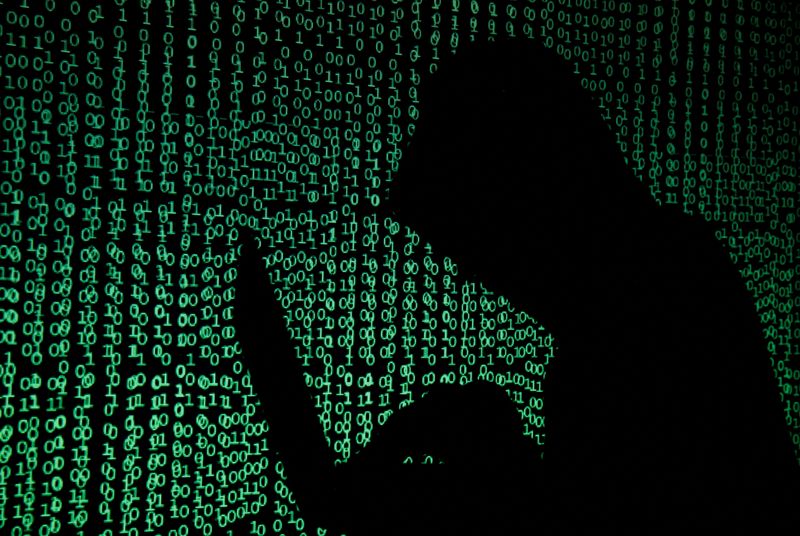 FILE PHOTO: A hooded man holds a laptop computer as cyber code is projected on him in this illustration picture taken on May 13, 2017.