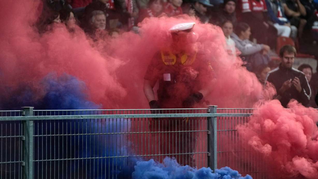 A policeman is engulfed in colored smoke from smoke bombs thrown onto the pitch during the women's Champions League opening phase soccer match between FC Bayern Munich and Manchester City in Munich, Germany, Tuesday, Sept. 22, 2026.
